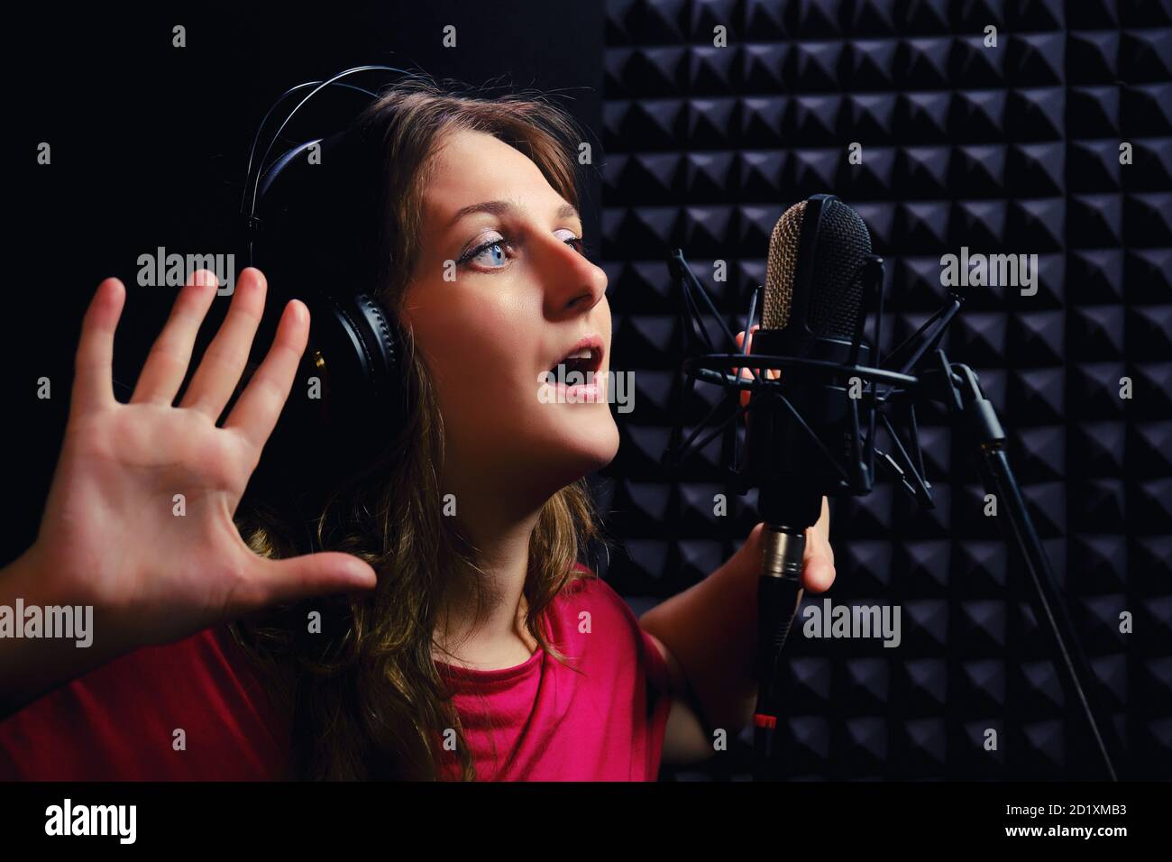 Chica una canción en los auriculares con las manos hacia arriba. Una joven  con ropa roja canta en el estudio de grabación. Músico en estudio de  grabación, primeros planos Fotografía de stock -