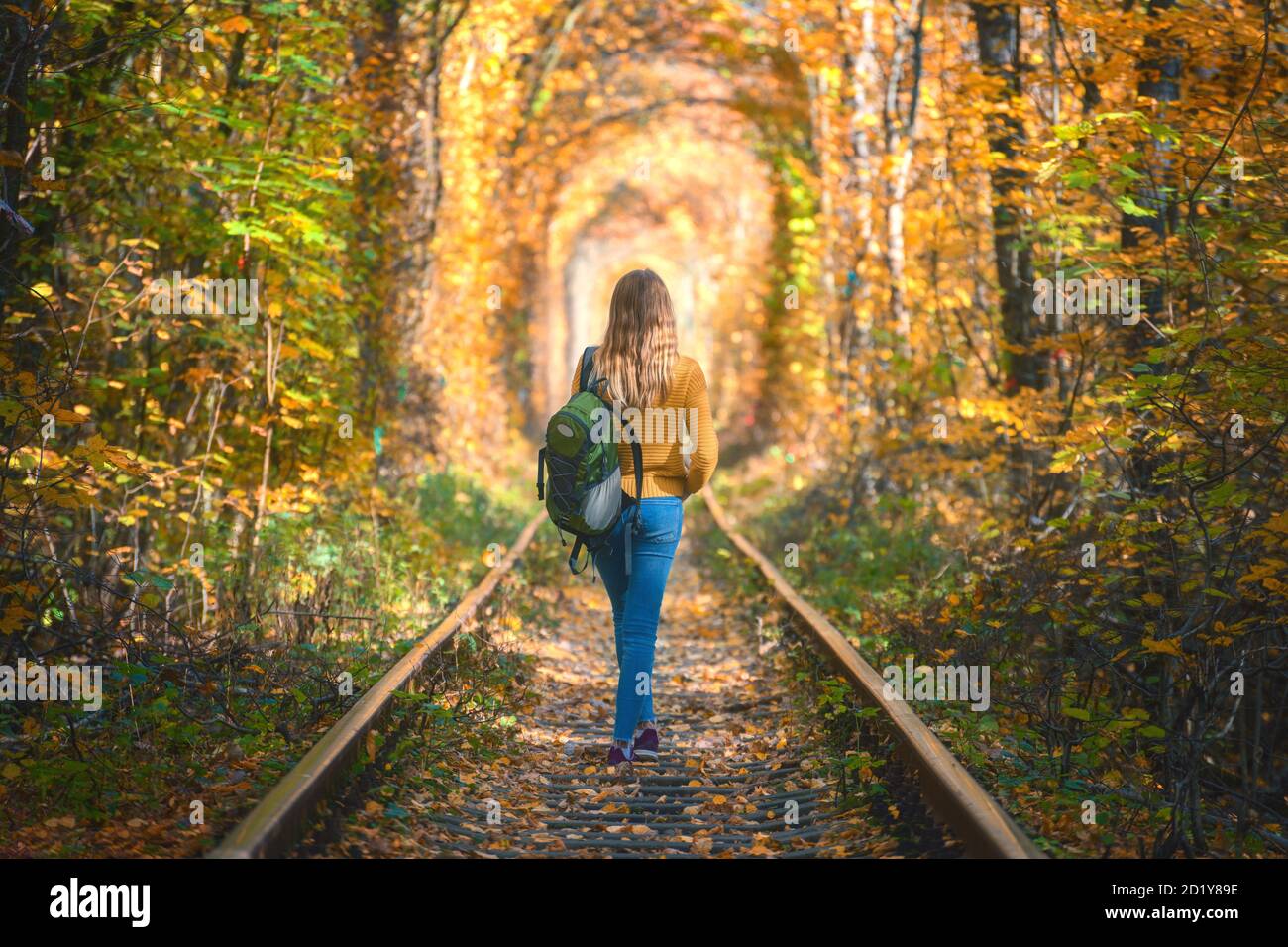Mujer joven caminando por el ferrocarril en un túnel de árboles en otoño Foto de stock