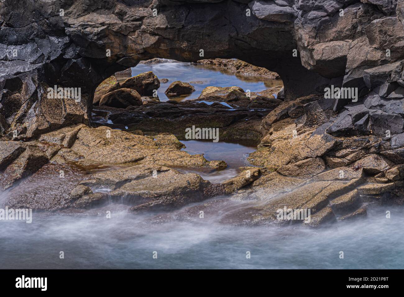 Un arco de piedra junto al mar muestra aguas tranquilas y borrosas detrás. Foto de stock