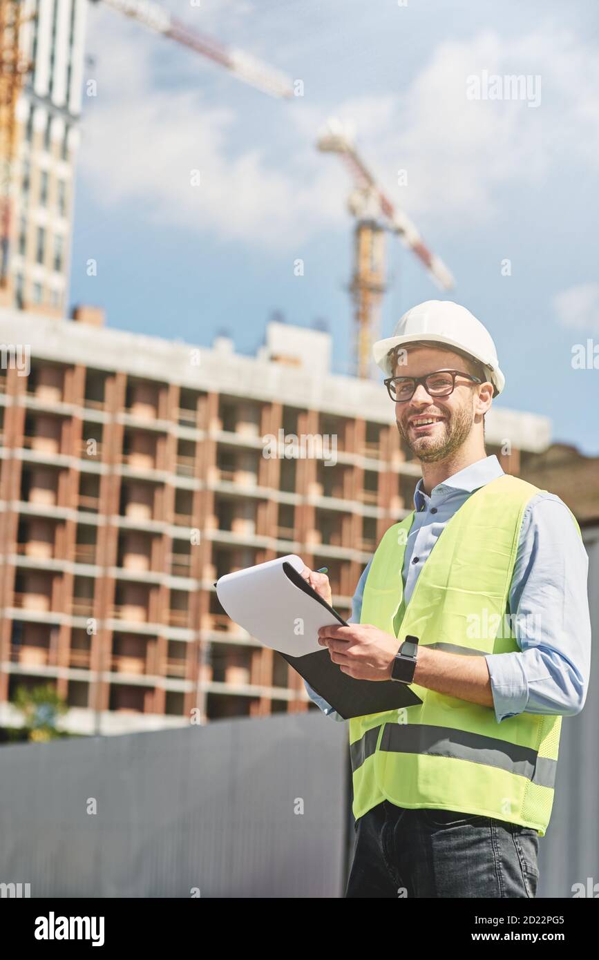 Buen feliz ingeniero civil o de la construcción con casco mirando y sonriendo mientras inspeccionan el sitio de construcción y hacen algunos Fotografía de stock - Alamy