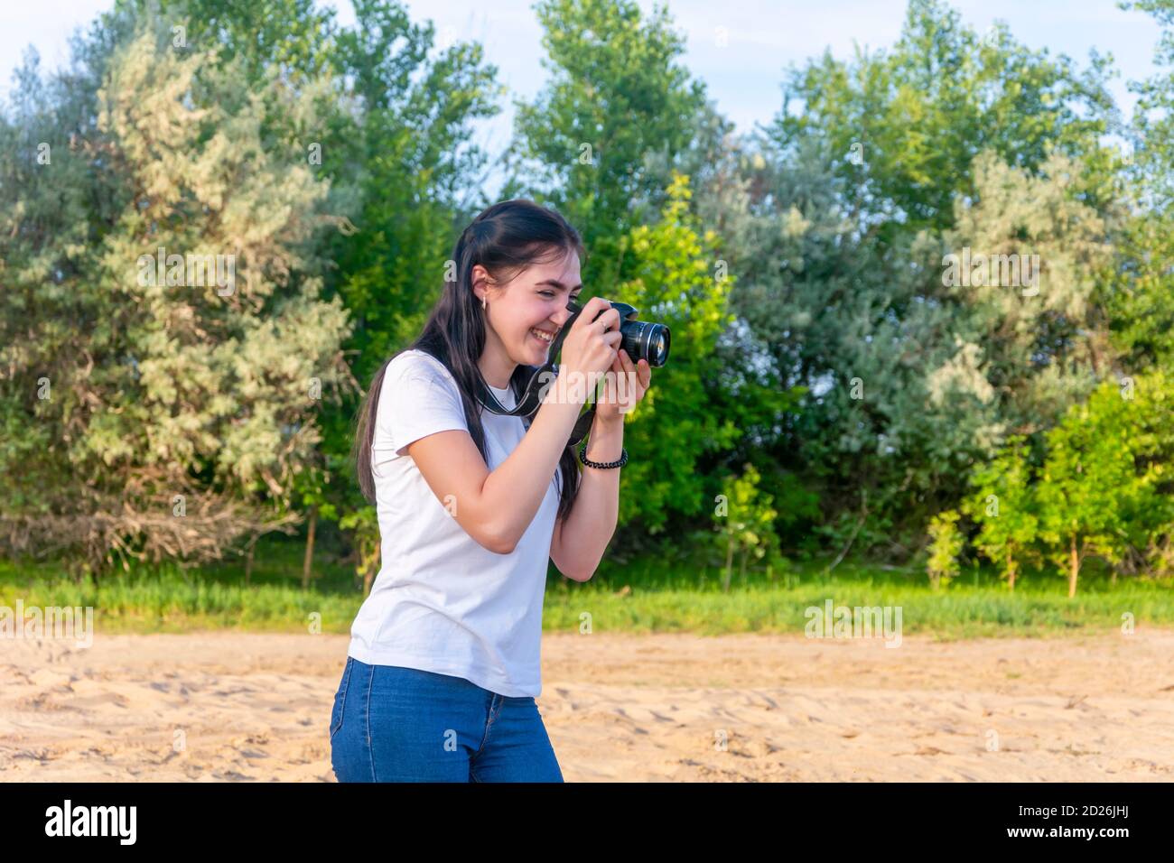 Mujer fotógrafa profesional en el trabajo. Tomar fotos al aire libre en el parque. La morena mira la cámara y se ríe. Enfoque selectivo. Foto de stock