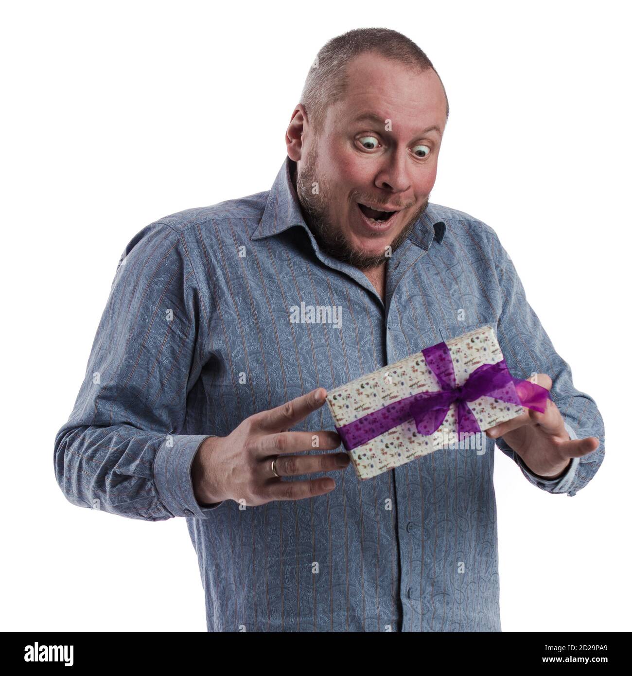 actor emocional hombre en una camisa gris con una caja con un regalo en las manos posando sobre un blanco fondo en el estudio Foto de stock