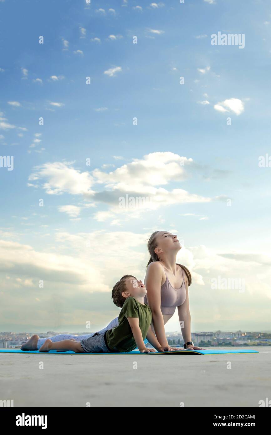 Madre e hijo haciendo ejercicio en el balcón en el fondo de una ciudad durante el amanecer o el atardecer, concepto de un estilo de vida saludable Foto de stock