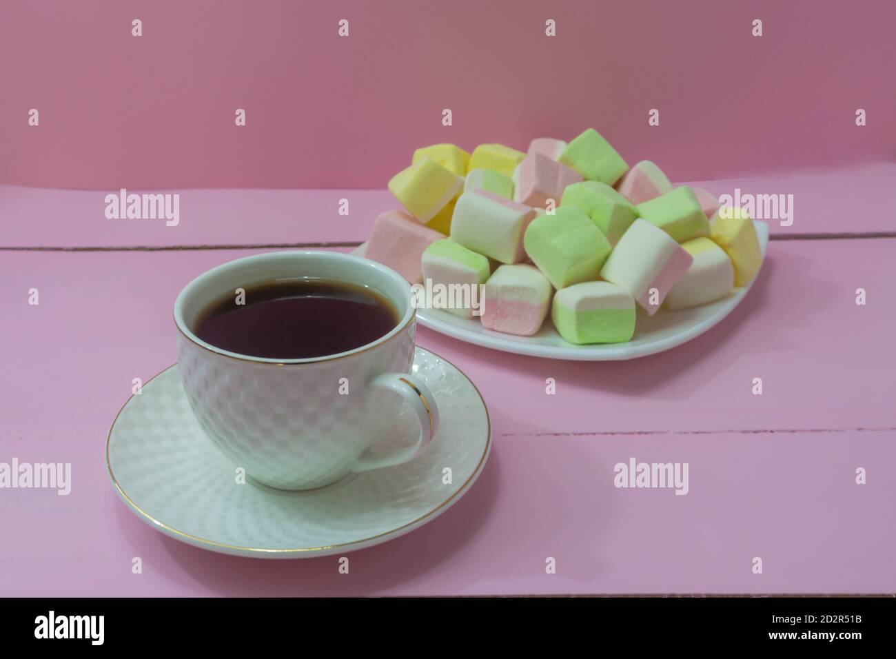 Taza de café sobre mesa de madera rosa y un montón de malvaviscos para el desayuno. Ternura por la mañana, positivo, buen humor. Foto de stock