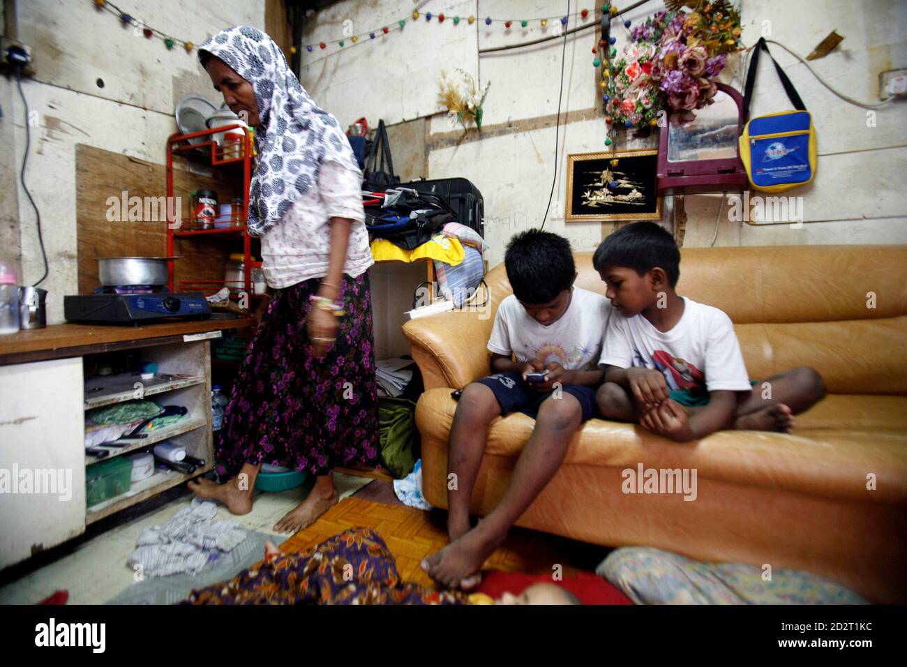 Los refugiados de Myanmar de la minoría étnica rohingya, Yusuf Salim (L),  9, y su hermano Sulaiman, 7, juegan un juego en un teléfono móvil mientras  su abuela, Jamilah Muhammad, se prepara