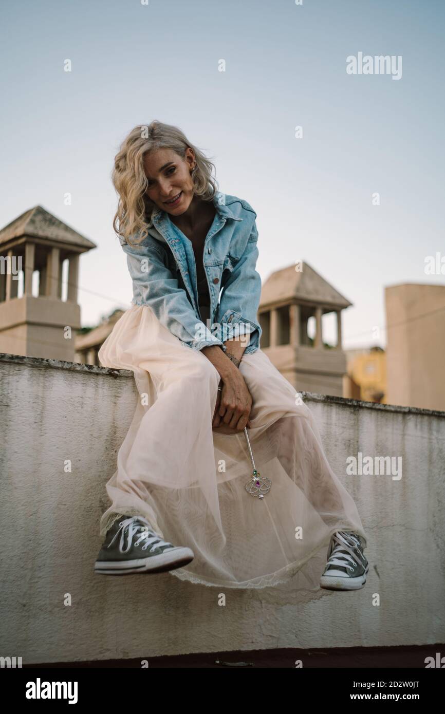 Mujer en chaqueta vaquera y pelo relajante en la ciudad de la terraza por la noche y mirando a la cámara Fotografía de stock - Alamy