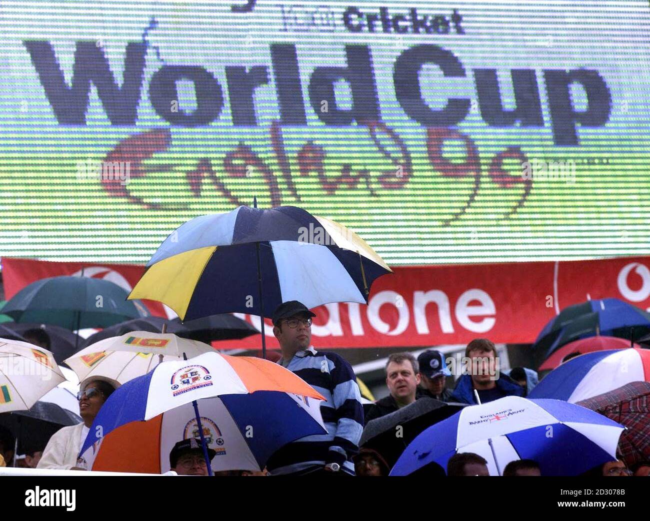 Los aficionados al cricket ponen sus paraguas mientras la lluvia impide jugar durante un corto tiempo al comienzo del partido de apertura de la Copa Mundial de Cricket de 1999, entre Inglaterra y Sri Lanka, en el campo de cricket Lord's de Londres. Foto de stock