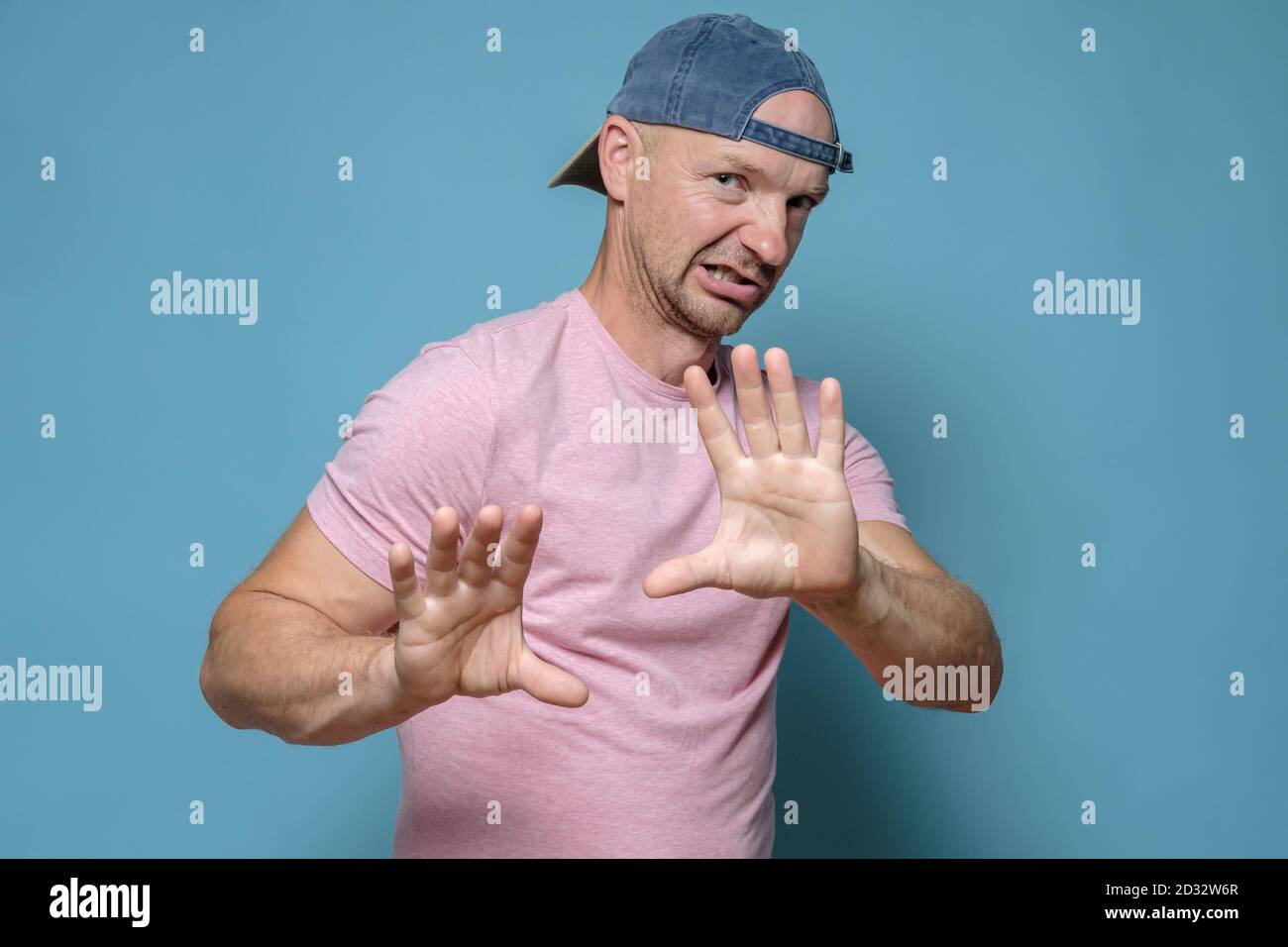 Hombre en una gorra y una camiseta rosa hace un gesto de parada, mira la  cámara con hostilidad y disgusto Fotografía de stock - Alamy