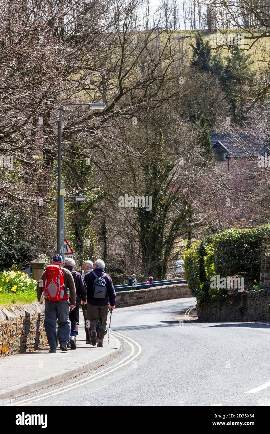 Un grupo de caminantes o excursionistas caminando por una carretera en el pueblo de Hope del Distrito de los Picos, Derbyshire, Inglaterra, Reino Unido Foto de stock