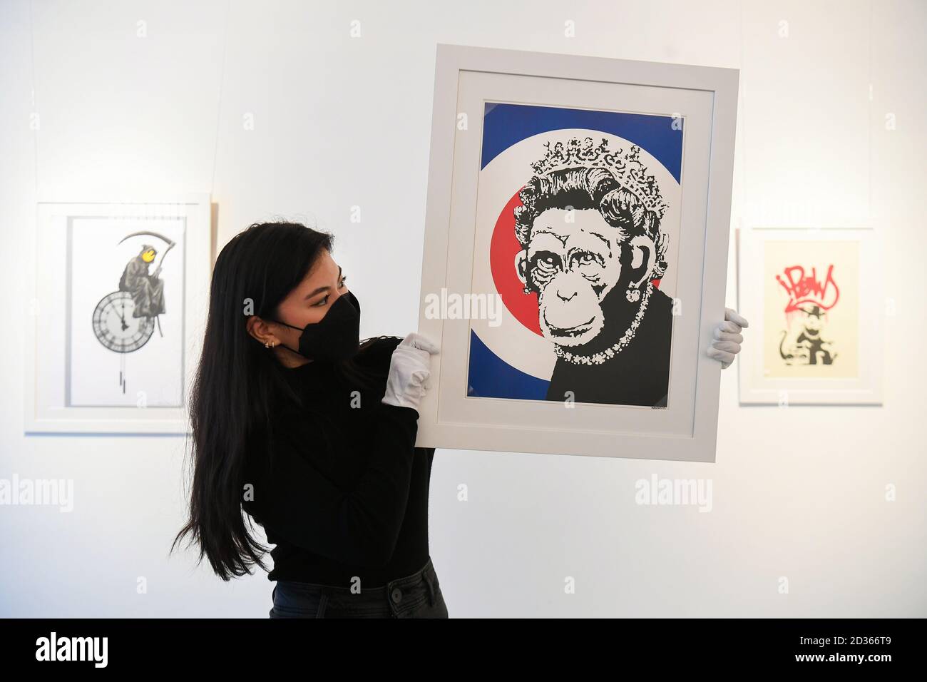 Sophia Shim, asistente de la galería, tiene una edición limitada de Monkey Queen (2003) de Banksy, junto a las copias de edición limitada de Grin Reaper (2005, izquierda) y Gangsta Rat (Roja) (2004, derecha), parte de la exposición 'Catch Me If You Can', en la Galería HOFA en Mayfair, Londres. Foto de stock