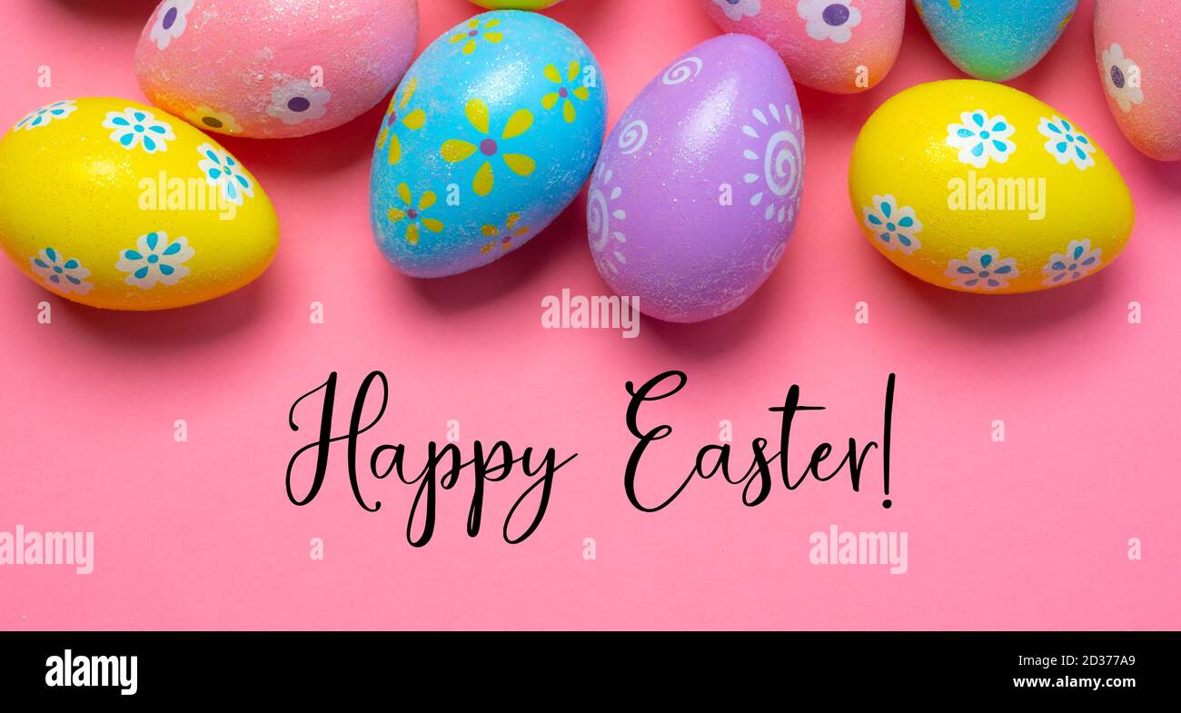 Coloridos huevos de Pascua sobre fondo rosa con saludo Foto de stock