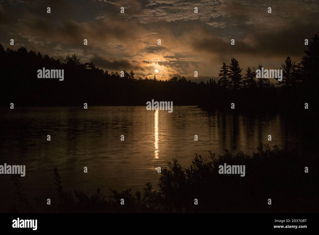 La luna se eleva después de que una tormenta ha pasado, sobre un pequeño lago en el norte de Ontario. Foto de stock