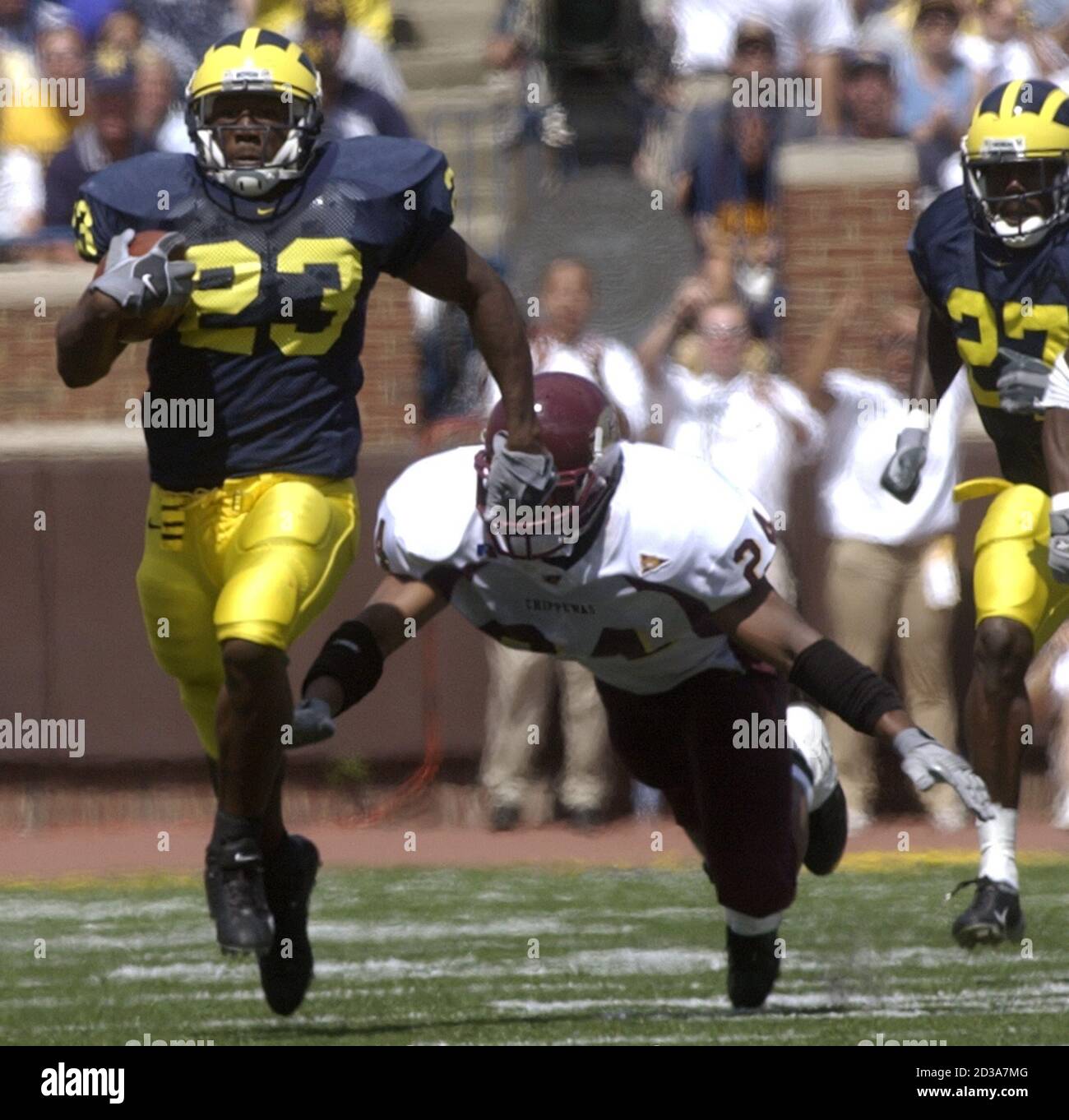 La Universidad de Michigan corriendo atrás Chris Perry (23) lleva la pelota por 33 yardas antes de ser tripped para arriba por el Central Michigan James King (24) en el tercer cuarto del juego en el estadio de Michigan en Ann Arbor, 30 de agosto de 2003. Michigan venció a Central 45-7. REUTERS/Rebecca Cook RC Foto de stock