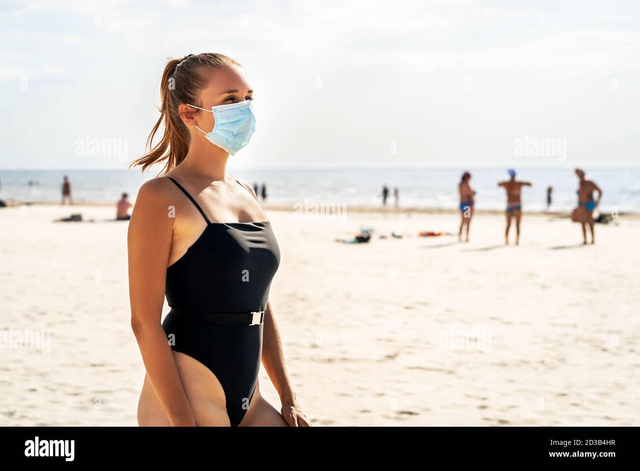 Gente en la playa durante el virus de la corona. Mujer que usa una máscara para protegerse del coronavirus. Covid, viaje, vacaciones y turismo concepto. Foto de stock