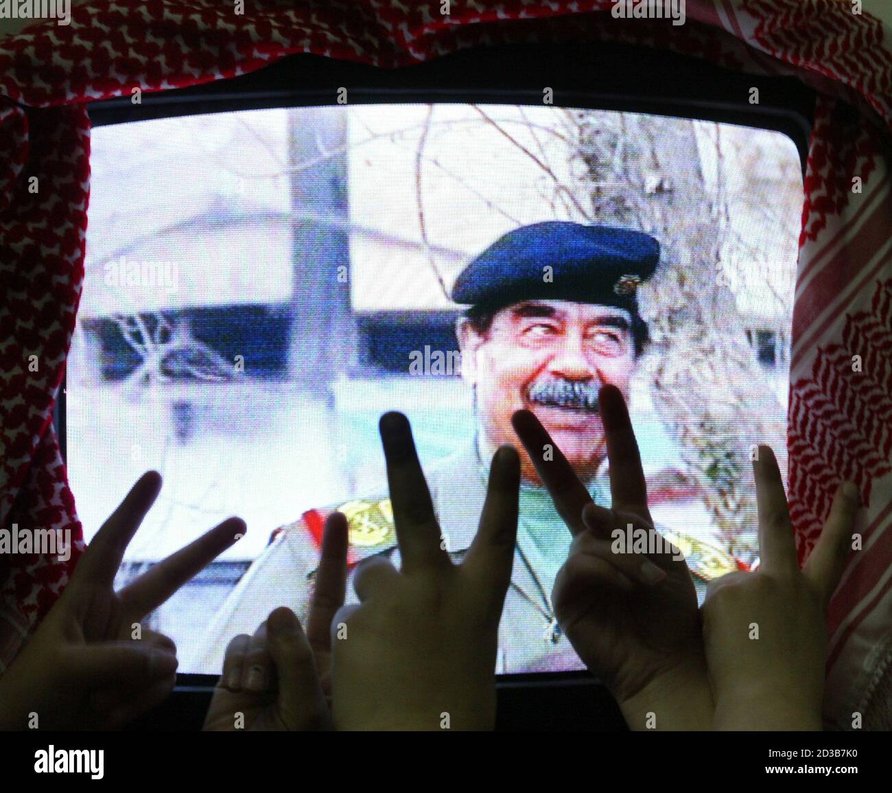 Los iraquíes que viven en Jordania hacen señales de victoria y animan al Presidente Saddam Hussein, como lo ven en la televisión en Ammán el 4 de abril de 2003, en una visita a un barrio residencial de Bagdad. Saddam, vestido con un uniforme militar, fue moved por animar, cantando a los iraquíes. No había manera de verificar cuándo se hizo la película. Saddam tiene una serie de dobles. REUTERS/Ali Jarekji WR/GB Foto de stock
