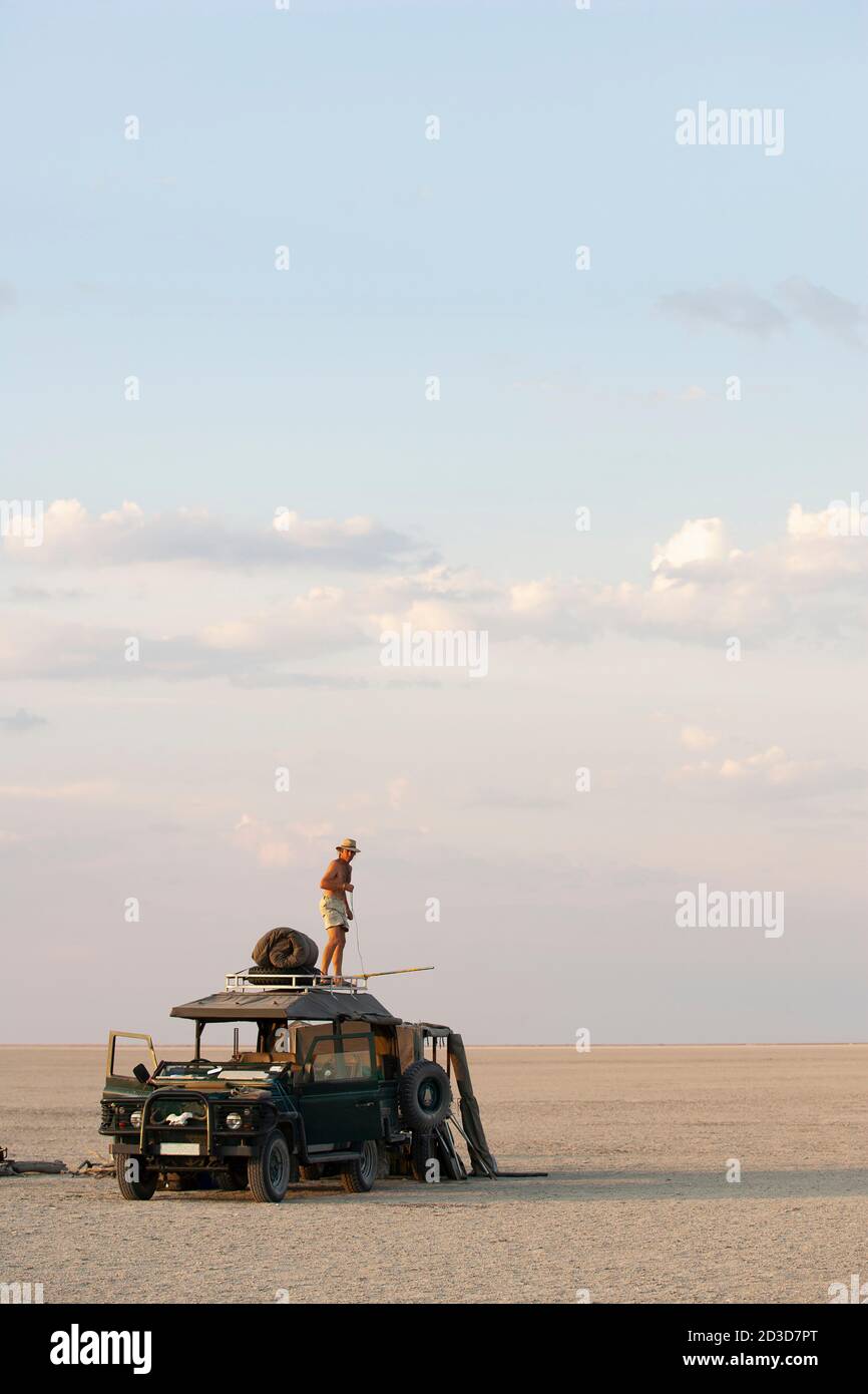 Hombre de pie en la parte superior de 4x4 estacionado en el Makadikadi Salt Pans en Botswana. Foto de stock