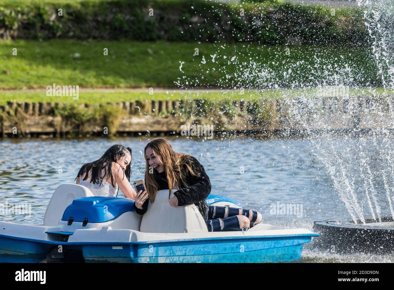 Una adolescente emocionada tomando un selfie en un pedalo como ella y su amiga se están empapando por el Spray de una fuente ornamental en el Trenance Boating Foto de stock