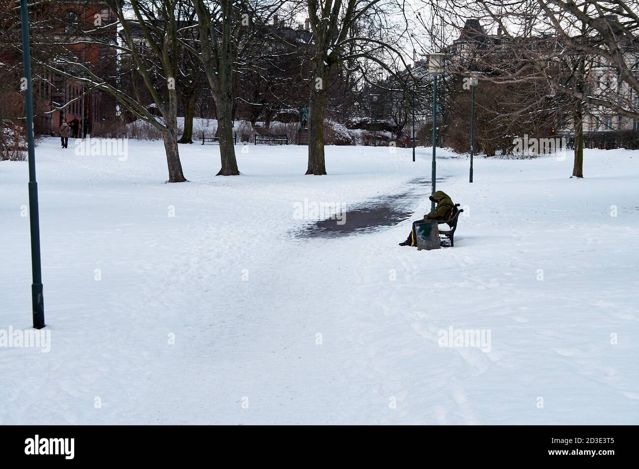 Persona sentada sola en un banco en una pequeña cubierta de nieve parque Foto de stock