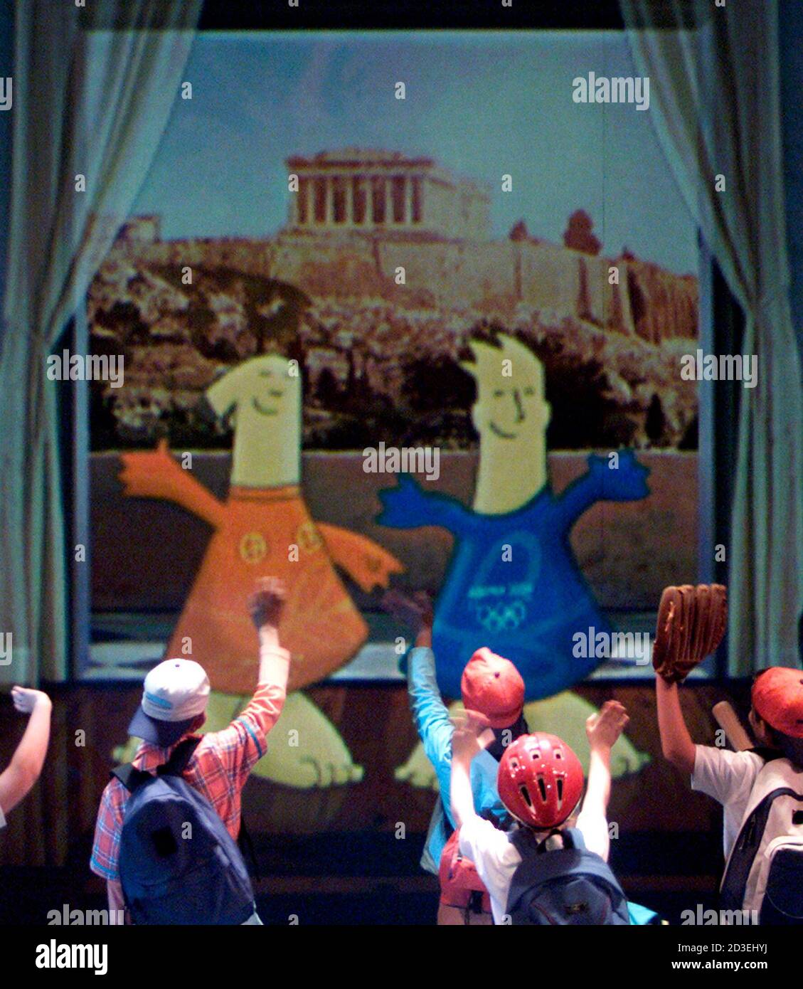 Los niños hacen una ola a las muñecas Athena y Phevos, las dos mascotas  para los Juegos Olímpicos de Atenas 2004 como se representan en una pared  de vídeo durante la ceremonia