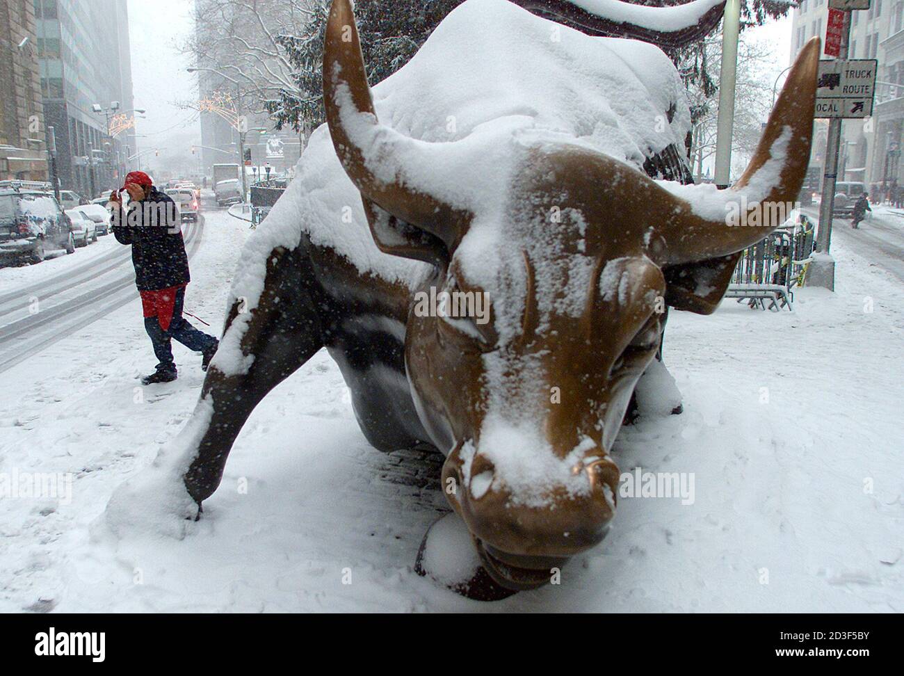 Un hombre protege su rostro de la nieve soplada mientras pasa por una  escultura cubierta de nieve de un toro en el distrito financiero de Nueva  York en Broadway, en el bajo