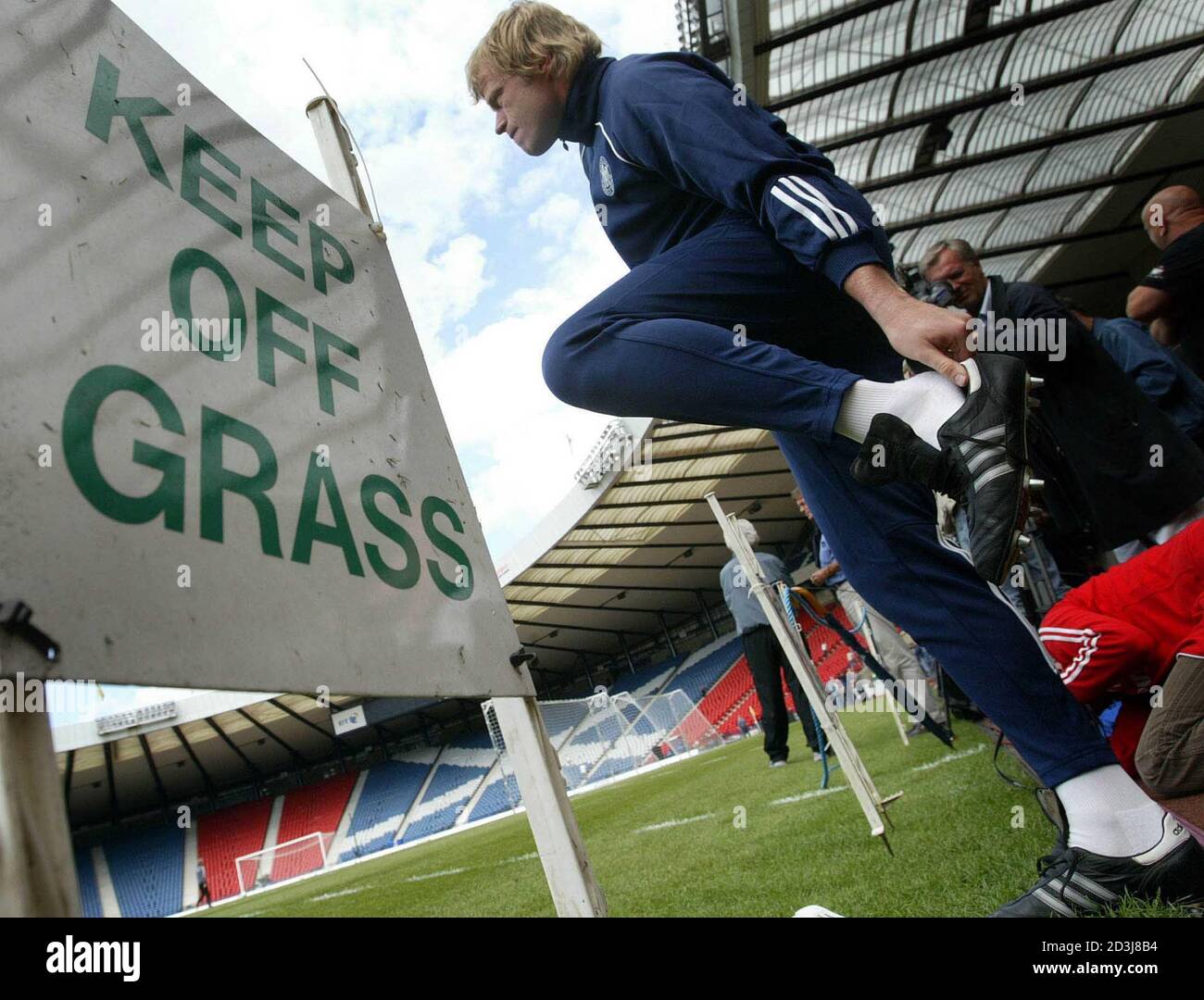 El capitán y portero de Alemania Oliver Kahn pone sus botas de fútbol  mientras entra en el campo junto a un cartel que dice 'Keep of grass' antes  de la sesión de