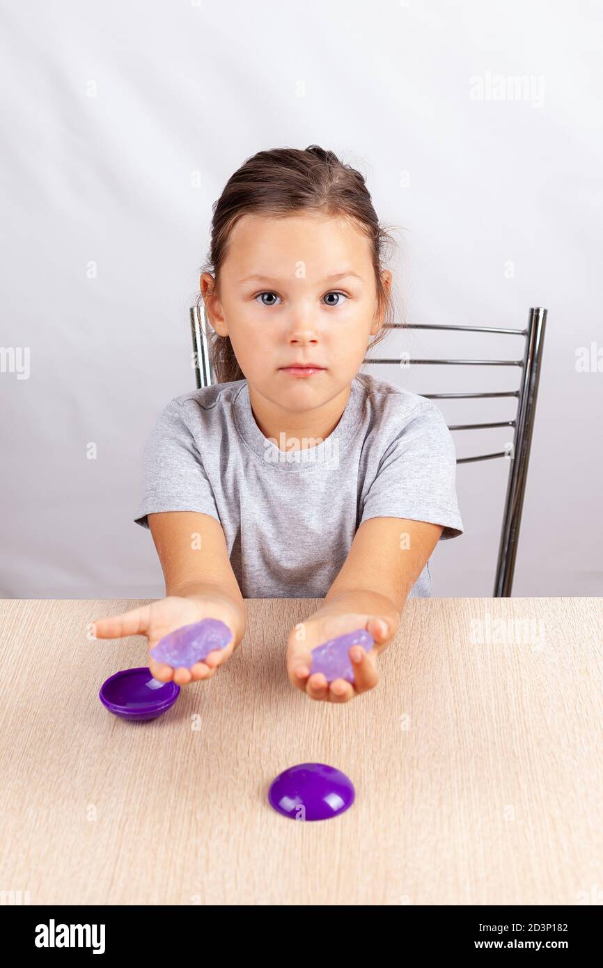el niño sostiene un juguete de slimo en sus manos y se sienta en la mesa, desarrollando habilidades motoras finas Foto de stock
