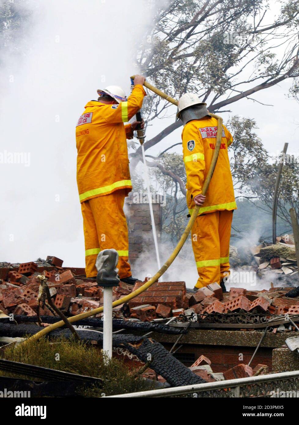 Los bomberos rurales vigilan los restos de una casa la mañana después de que fuera destruida por incendios en el suburbio de Engadine, al sur de Sydney, 9 de octubre de 2002. El martes se quemaron alrededor de Sydney unos 47 incendios de arbustos y pastos, destruyendo 10 viviendas en Engadine y forzando la evacuación de 200 personas. REUTERS/Mark Baker MDB/RCS Foto de stock