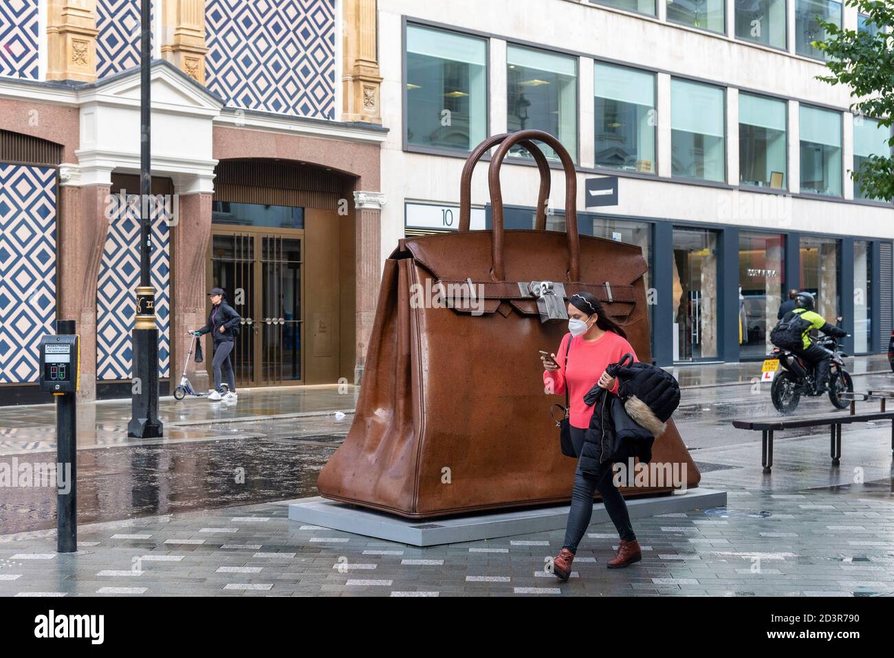 Una mujer que lleva una máscara pasa por un Kallliopi Lemos 'Bolsa de  aspiraciones' de acero dulce y acero inoxidable, una gigantesca escultura  de bolso de mano que se exhibe en la