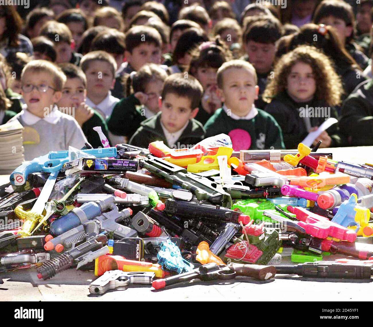 Decenas de niños guarderías argentinos se sientan frente a la pila de armas de juguete que entregaron a cambio de suministros escolares y juguetes educativos en la plaza de la
