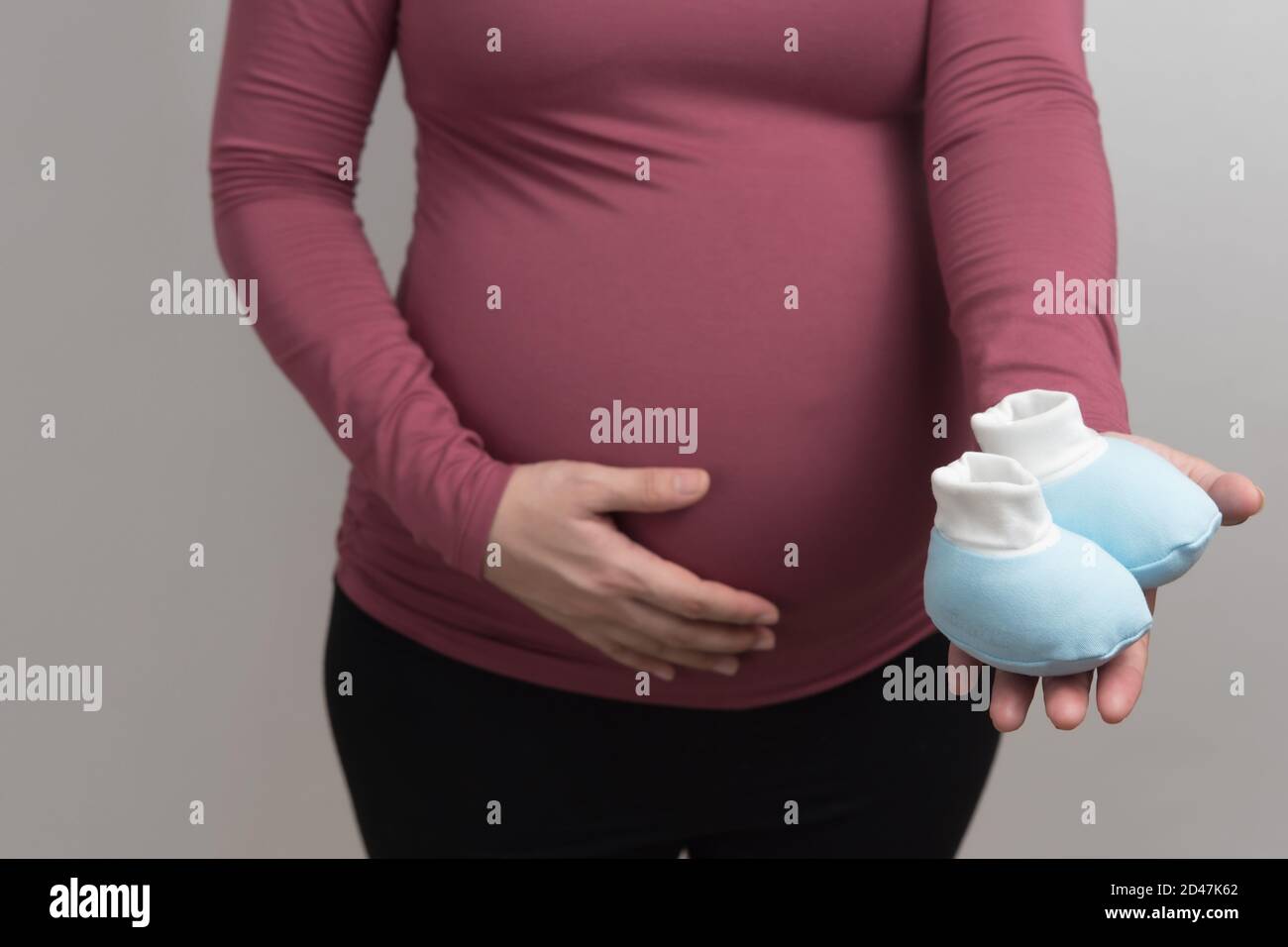 Primer plano cuerpo de mujer embarazada asiática con camiseta de manga larga  roja que sostiene el mono azul zapato bebé, retrato de luz de estudio y  espacio de copia en la espalda
