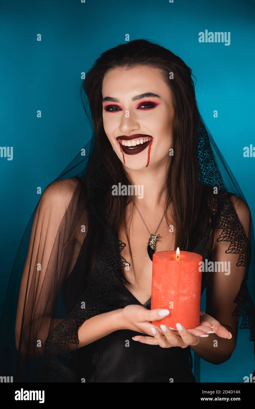 mujer en el velo con sangre en la cara sosteniendo la quema roja vela y  riendo en azul Fotografía de stock - Alamy