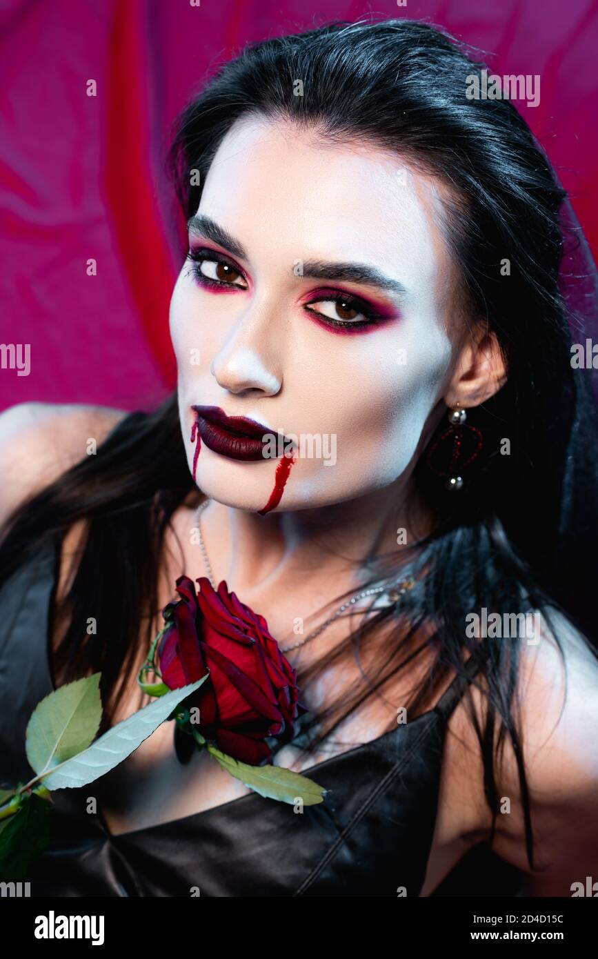 mujer joven pálida con sangre en la cara y rosa mirando en la cámara en  rojo Fotografía de stock - Alamy