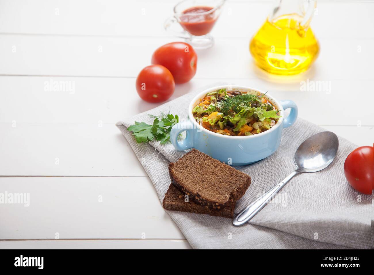 Sopa de frijoles y aceitunas con hierbas en un cuenco de cerámica, tomates, aceite de oliva y pan en una mesa de madera blanca. Copiar espas Foto de stock
