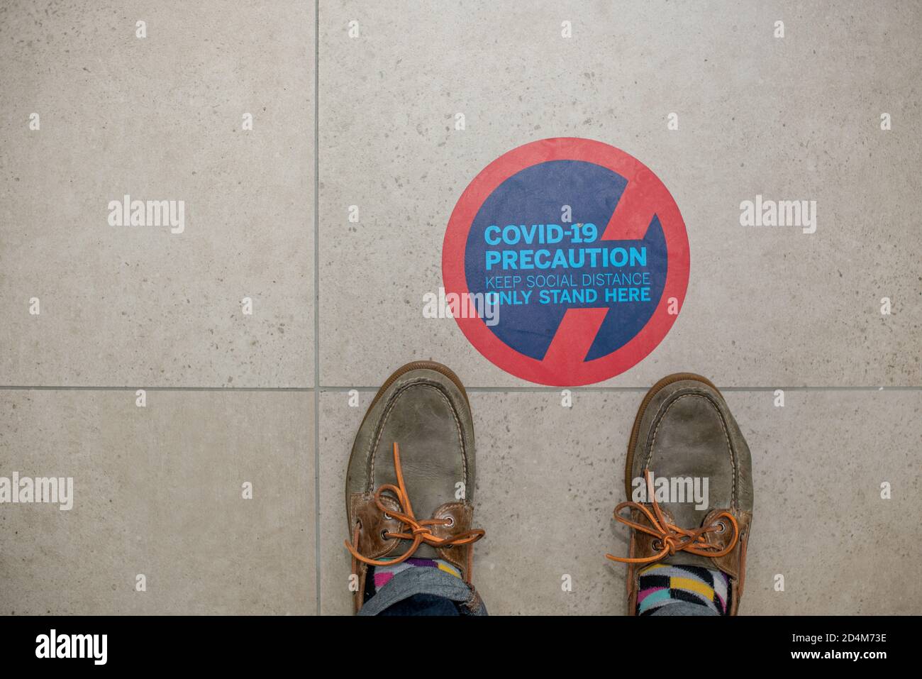 Señal de distancia social en el suelo con zapatos de pie al lado él Foto de stock
