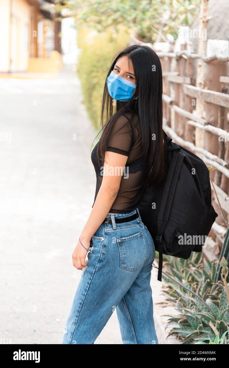 hermosa mujer latina joven con pelo largo negro, con su espalda caminando,  usando una máscara, blusa transparente con jeans y una mochila negra  Fotografía de stock - Alamy