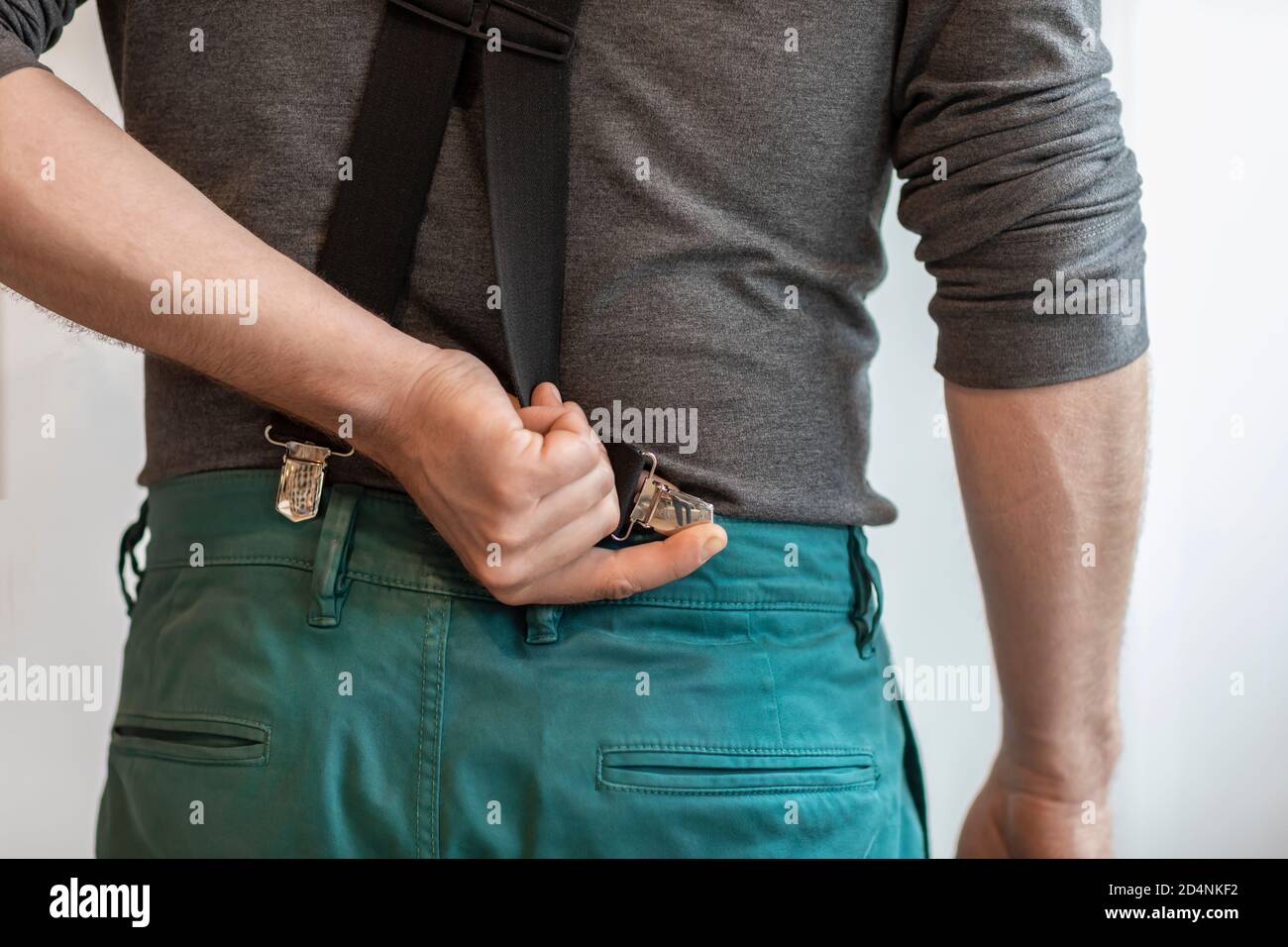 Un hombre sosteniendo un clip de sus suspenderos y sujetándolo a su pantalón  verde. Moderno estilo de moda formal de cintura baja. Primer plano de una  mano y ropa Fotografía de stock -