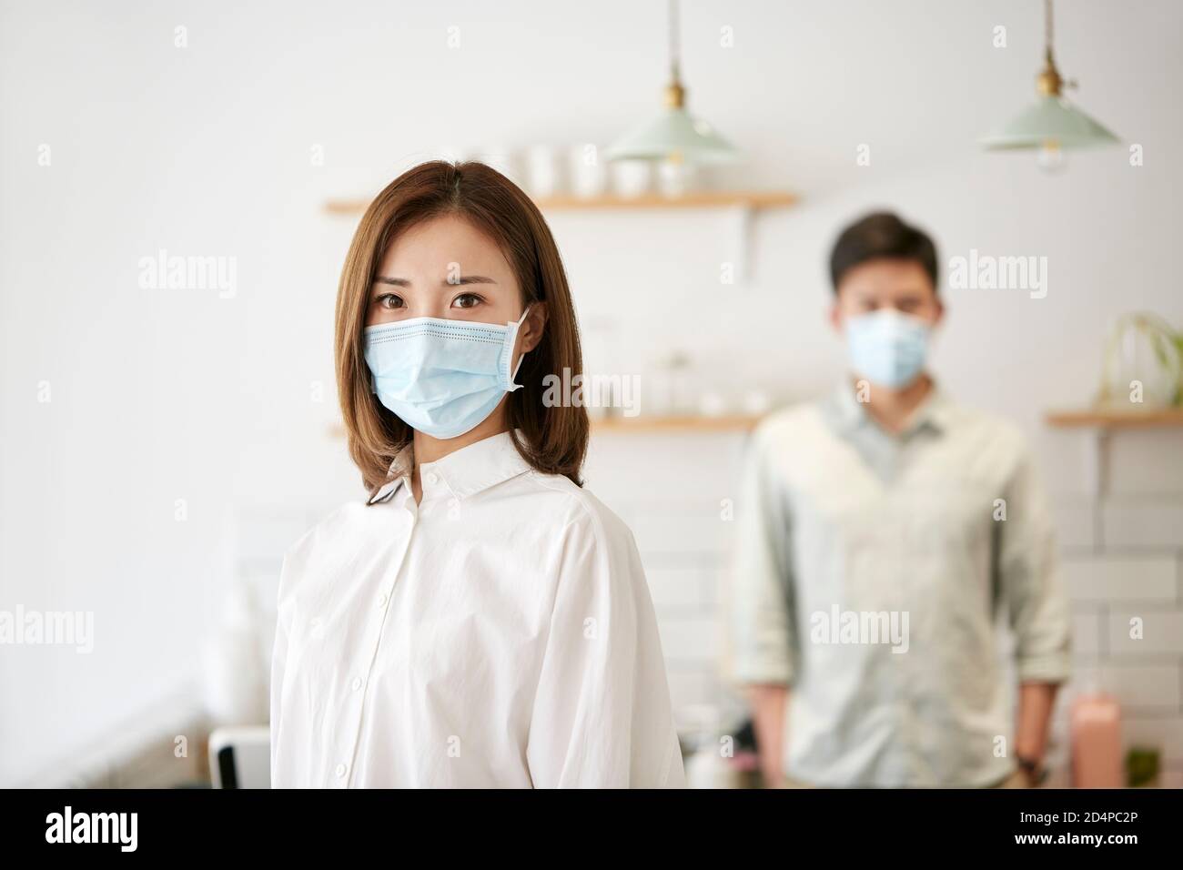 retrato de una joven mujer asiática con máscara mirando cámara con esposa en el fondo Foto de stock
