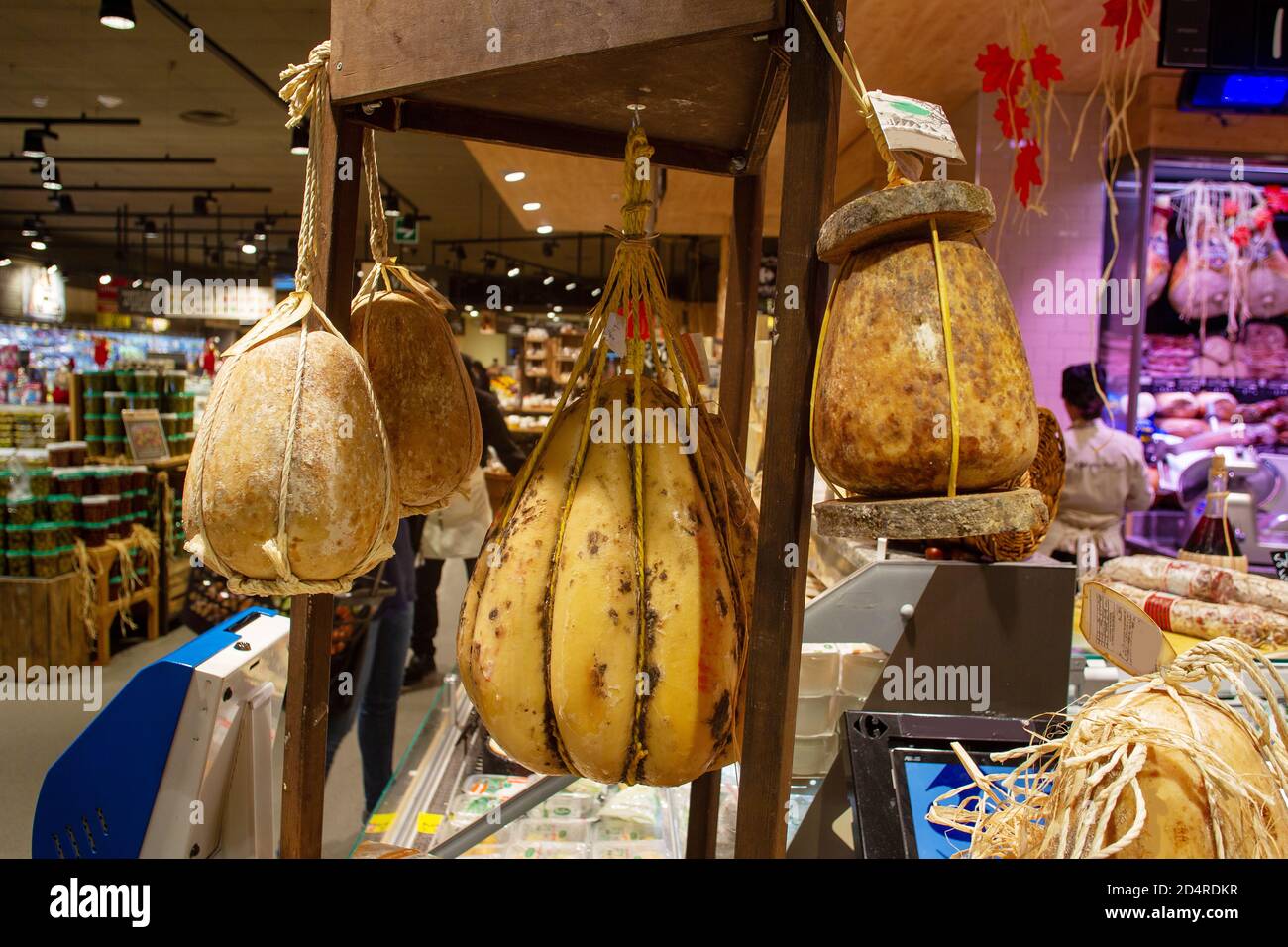 Colgando en las cuerdas, cavando en el cuerpo del queso, quesos deliciosos en un supermercado en Nápoles el hall de la tienda y la gente son Foto de stock