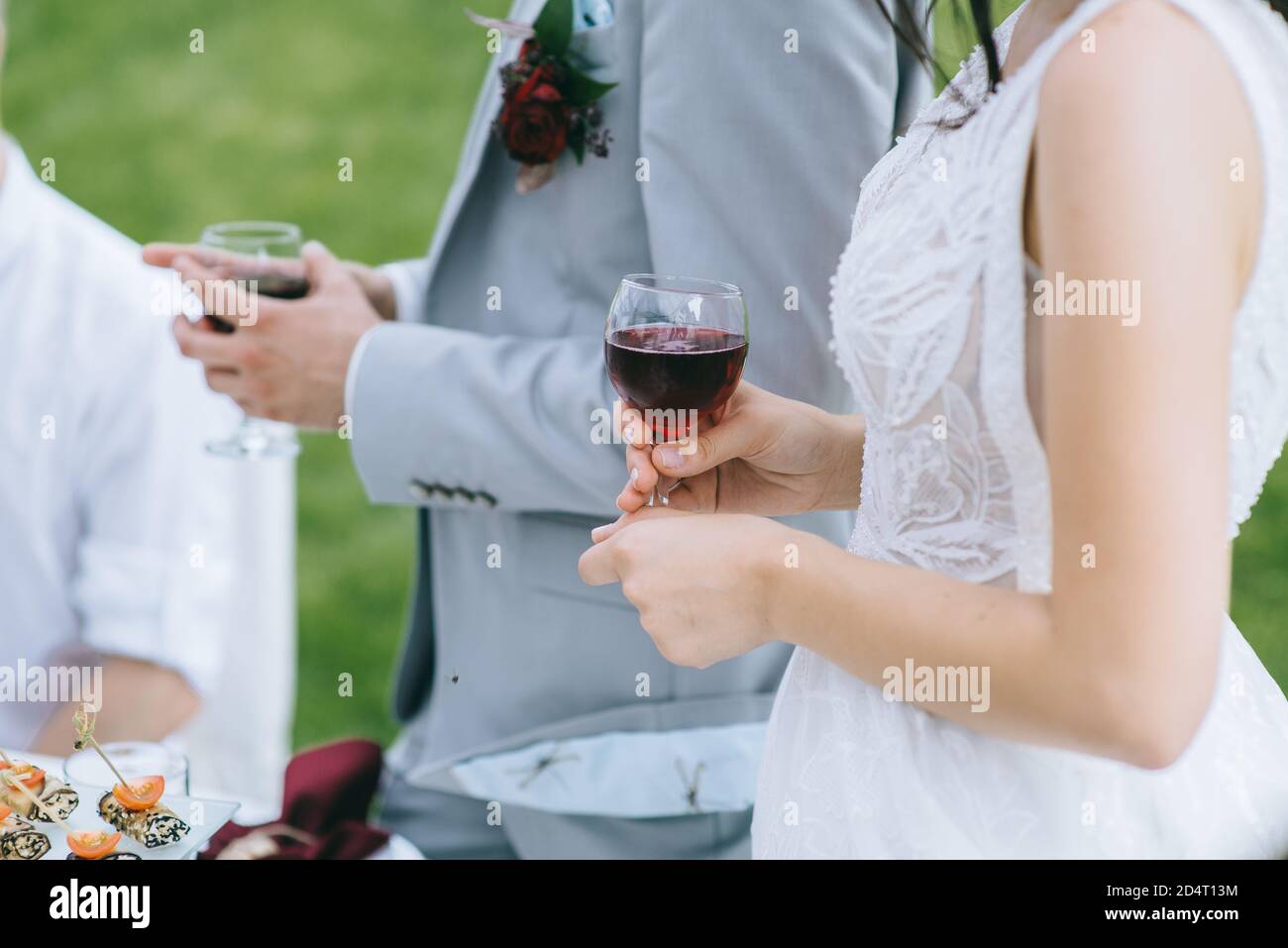 Primer plano de una copa de vino tinto en las manos de la novia vestida con un vestido blanco al aire libre. Foto de stock