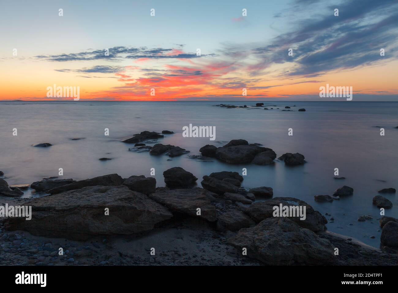 Puesta de sol al atardecer sobre la costa rocosa del mar Báltico. Cielo casi despejado y correa naranja a lo largo del horison. Estonia. Foto de stock