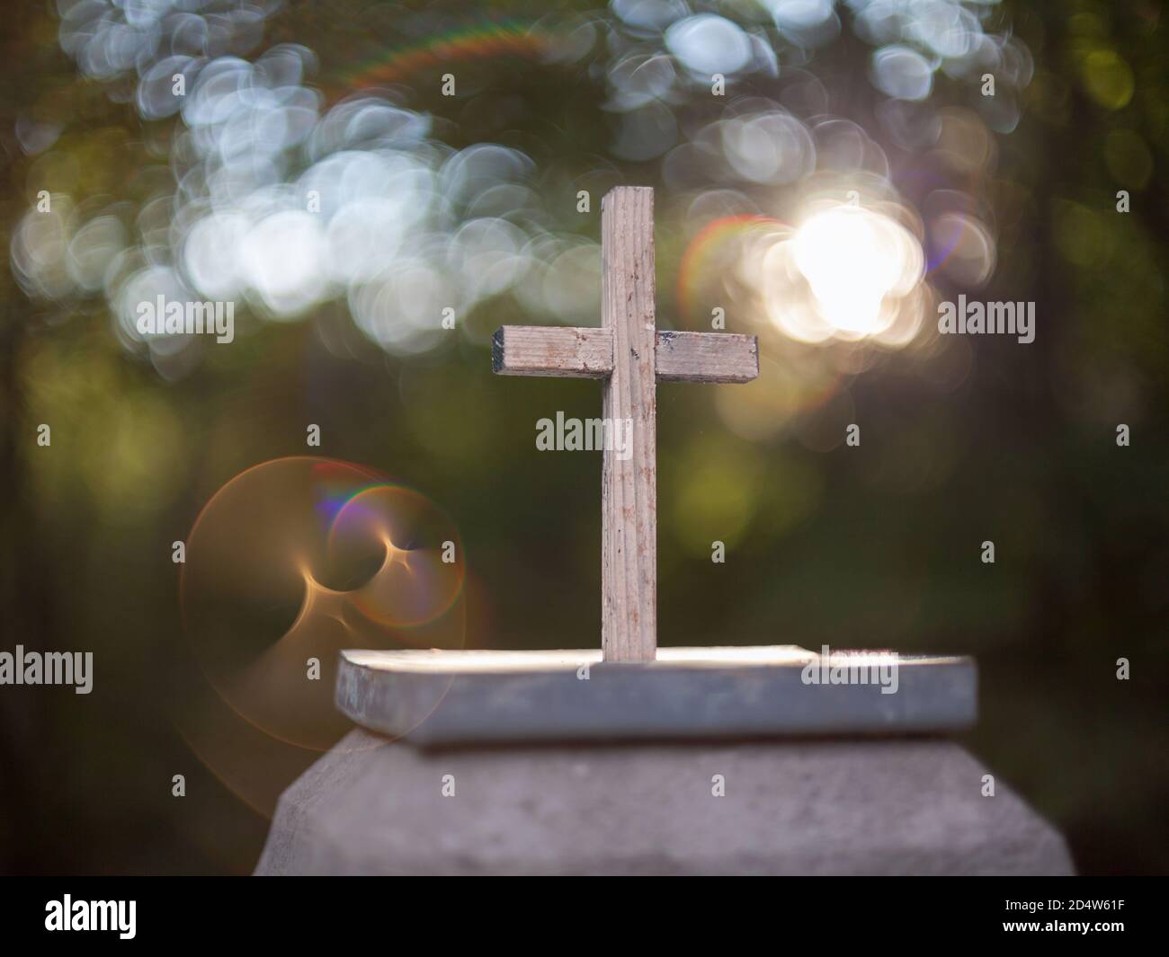 Pequeña cruz católica de madera sobre un pedestal de piedra con un fondo agradable y una reflexión inusual. Foto de stock