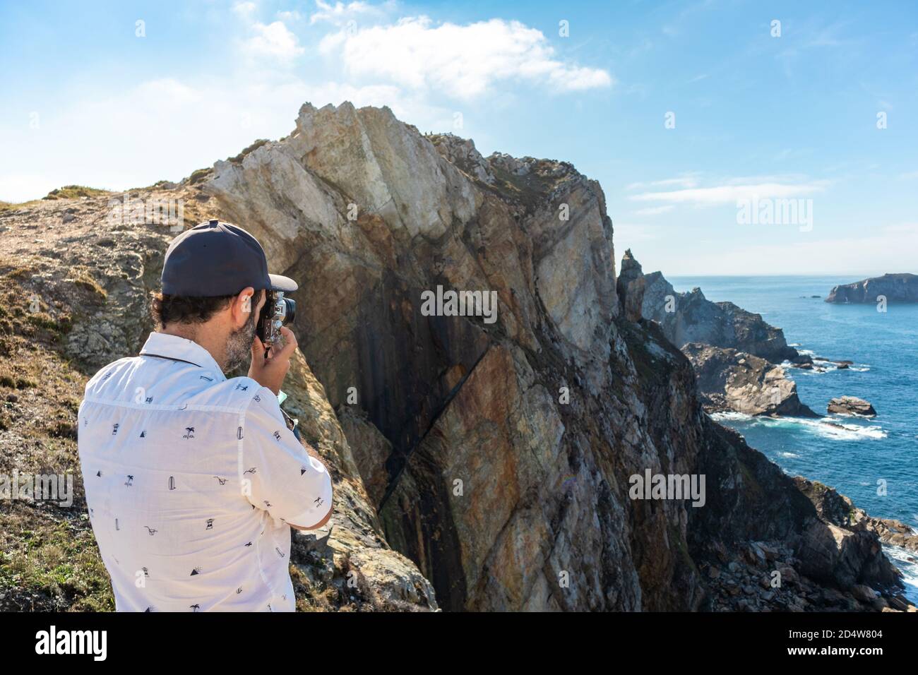 Turista masculino tomando fotos del océano en la cima de un acantilado  alto. Utiliza una cámara fotográfica de estilo retro. Horario de verano.  Cabo Peñas (Cabo de Peñas Fotografía de stock -