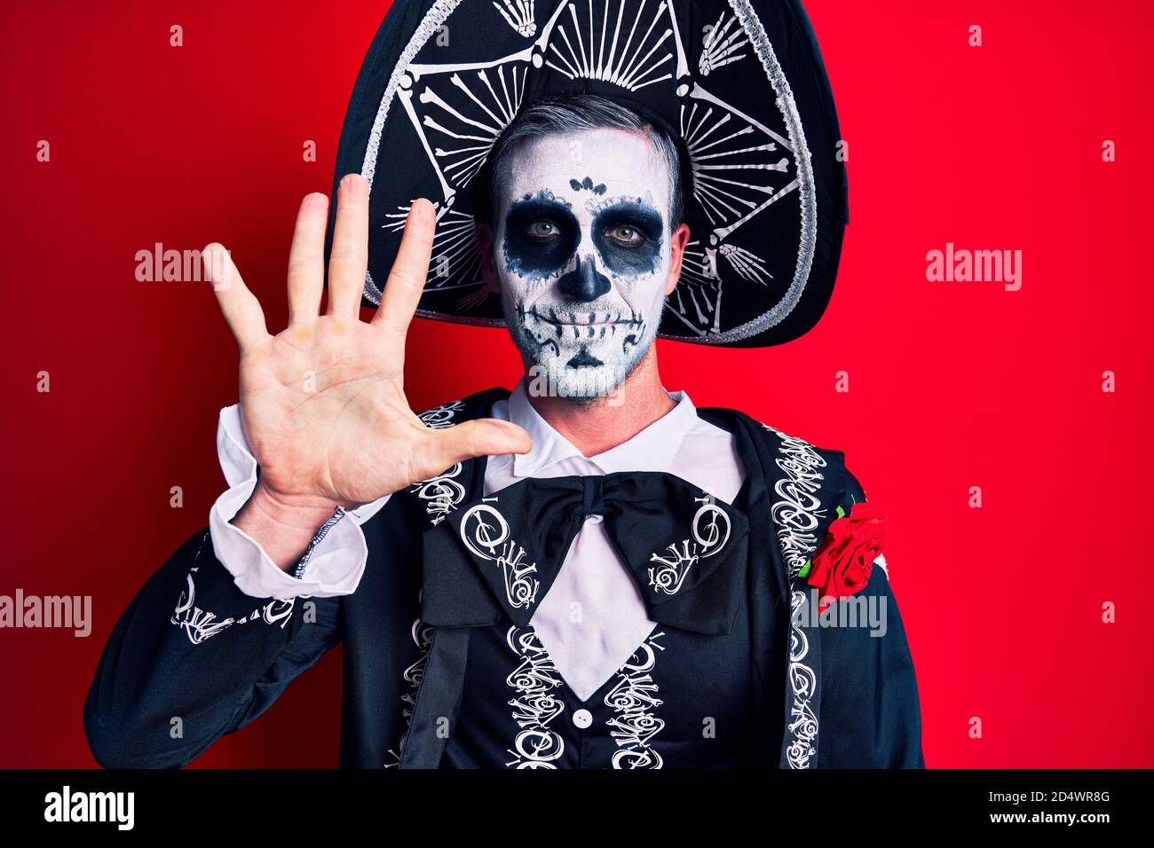 Hombre joven con traje mexicano de día muerto sobre rojo mostrando y señalando con los dedos número cinco mientras sonriendo confidente y feliz. Foto de stock