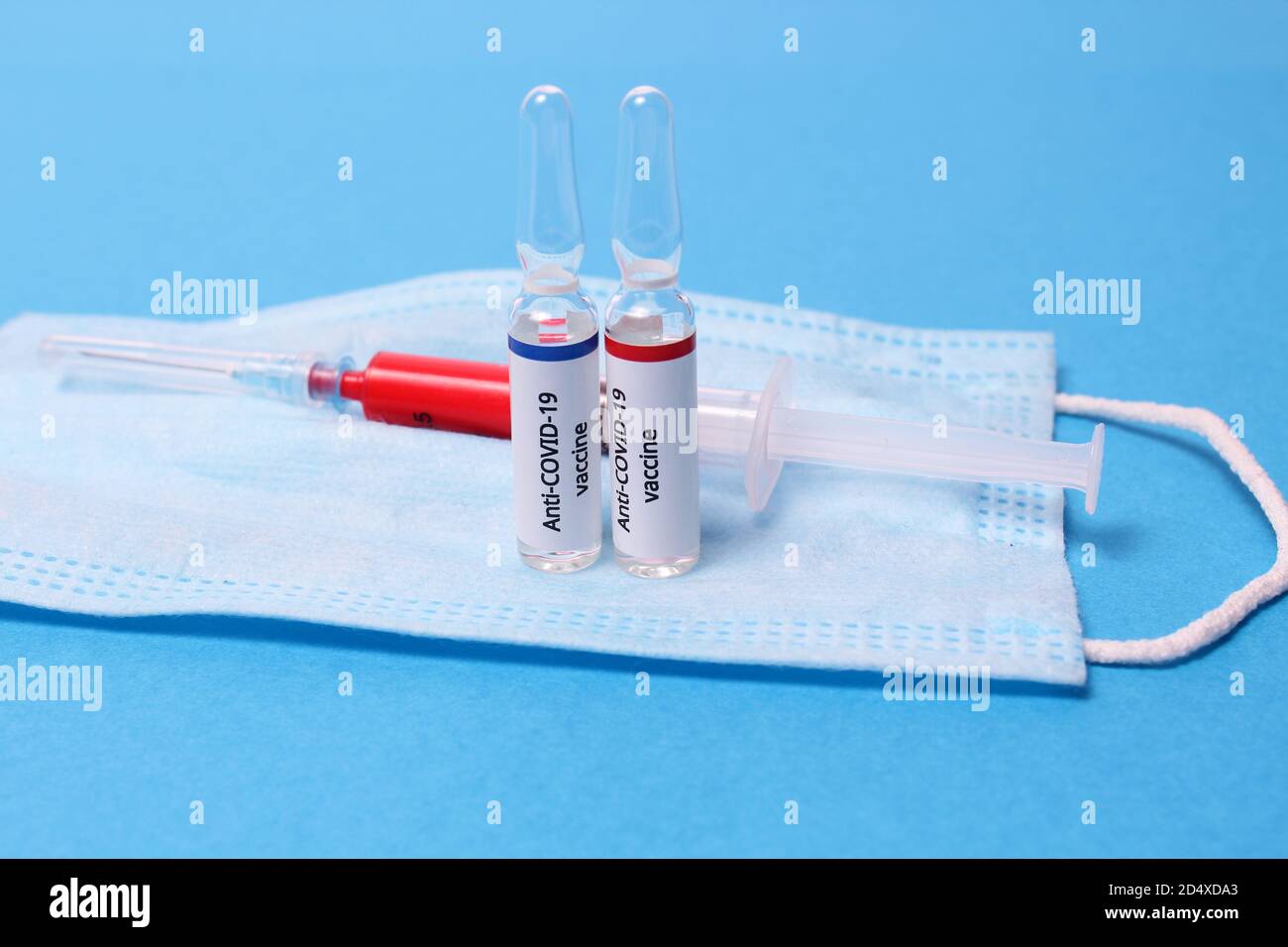Dos ampollas de medicamento con vacuna anticovid contra el sars y jeringa sobre máscara de protección sobre fondo azul Foto de stock