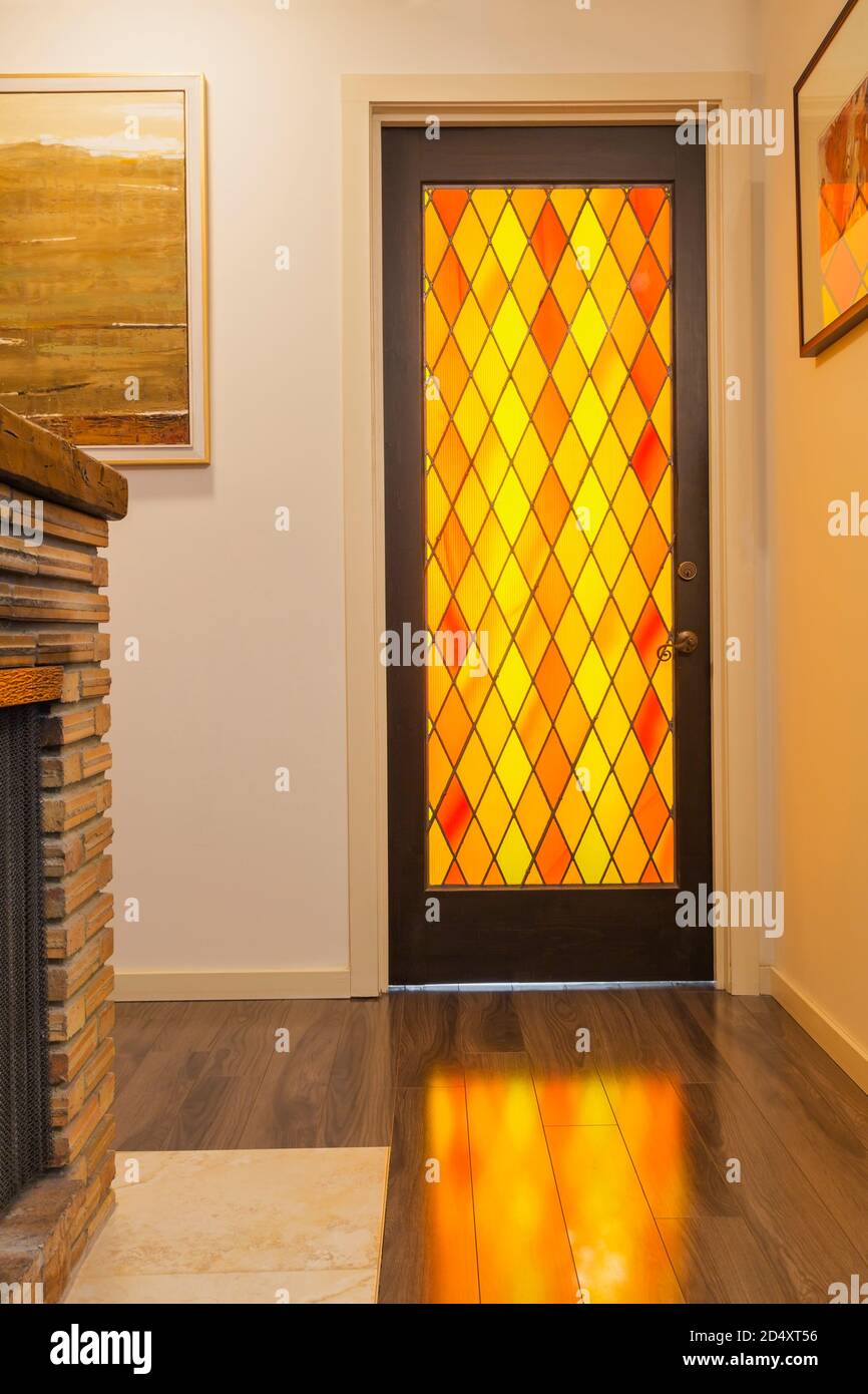 Puerta del dormitorio con paneles de vidrio de color naranja y amarillo retroiluminados en el pasillo del sótano dentro de una casa contemporánea decorada con pinturas. Foto de stock
