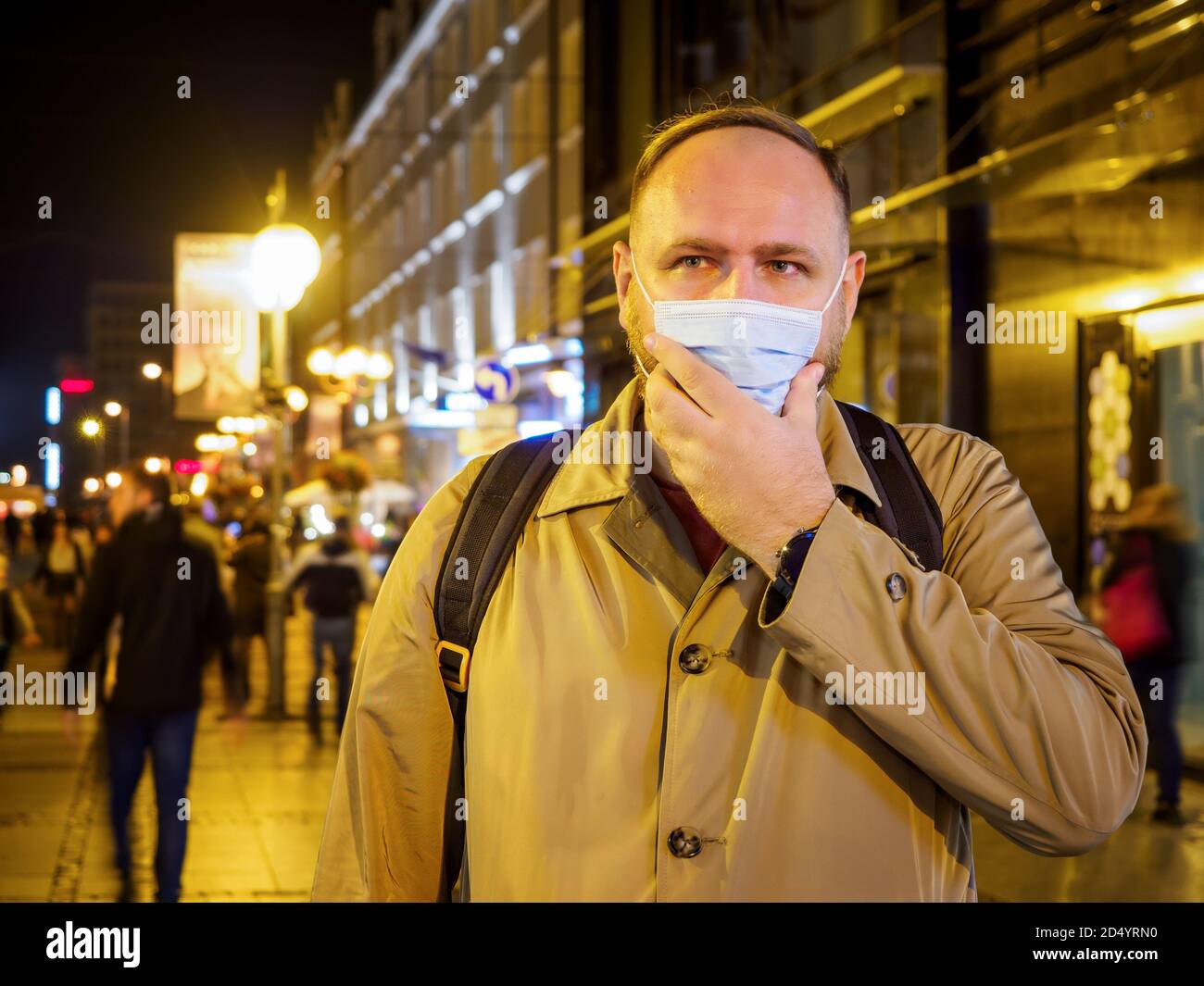 Hombre adulto con máscara caminando en una ciudad europea nocturna. La máscara es una cosa necesaria en la nueva realidad normal Foto de stock