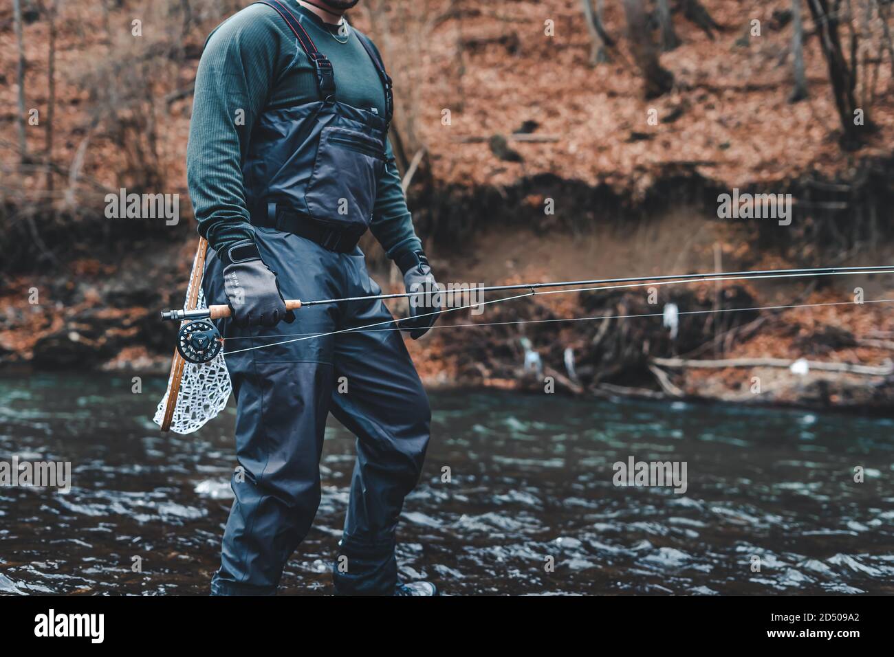 Pescador pesca con mosca en el río con caña, carrete y red de aterrizaje Foto de stock