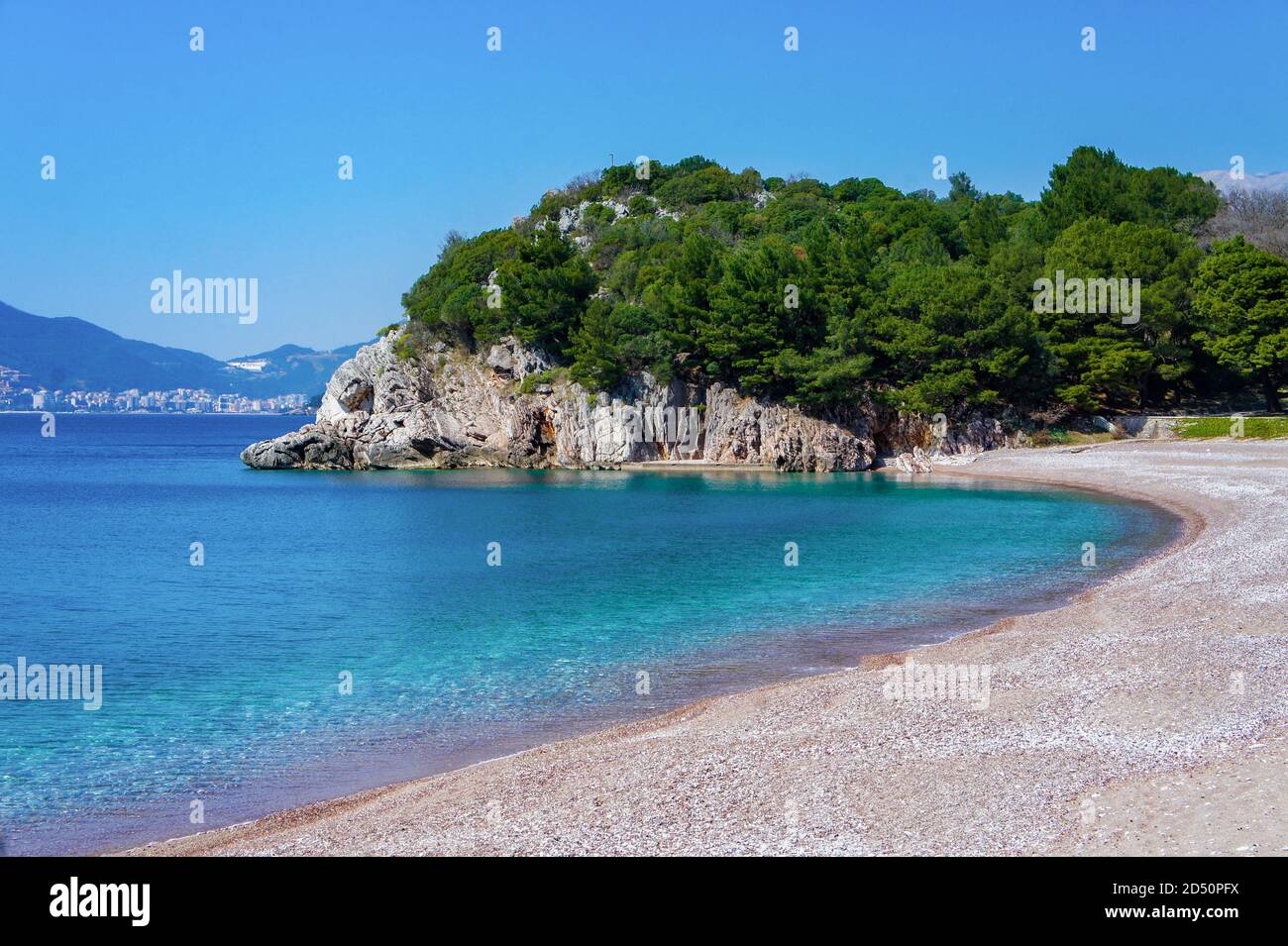 Mar Mediterráneo azul, playa con pequeñas guijarros de naranja, rocas con pinos verdes. Foto de stock