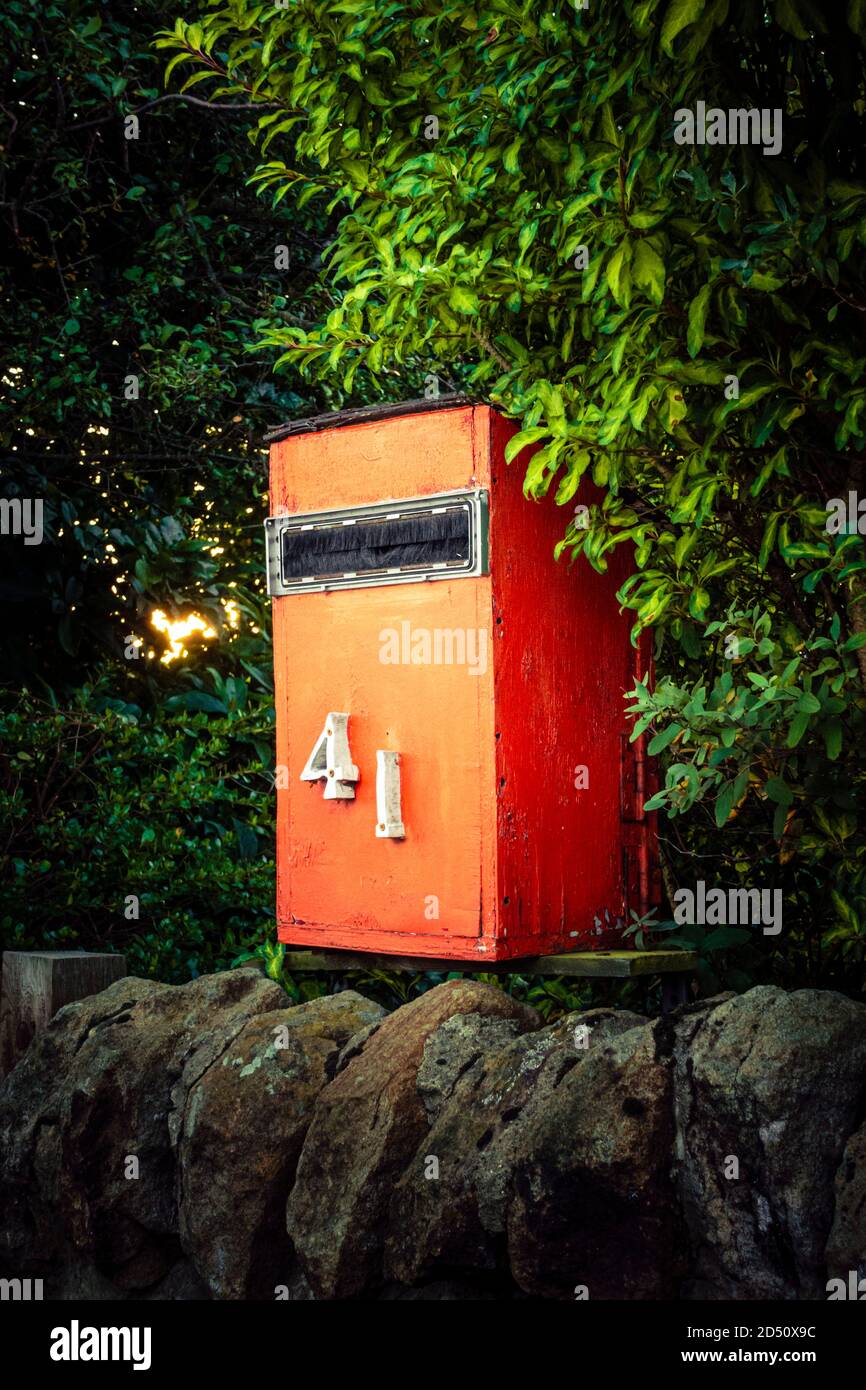 Casa hecha de madera roja caja de cartas o buzón de correo en una pared de piedra con árboles detrás Foto de stock