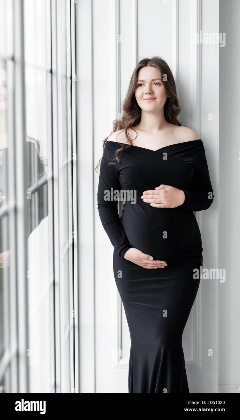 hermosa mujer embarazada joven con vestido negro oscuro se encuentra cerca  la ventana Fotografía de stock - Alamy